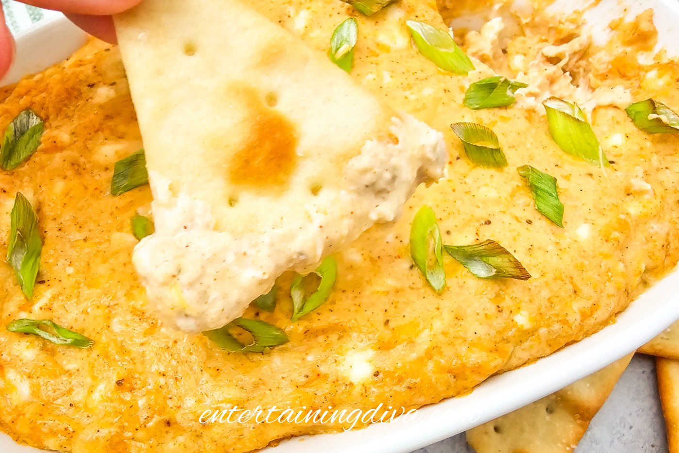 A tortilla chip with crab dip on it above a baking dish of baked crab dip