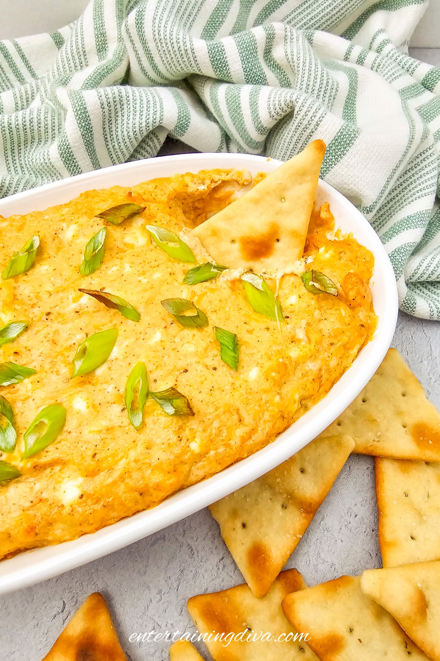 baked hot crab dip with cream cheese in a white baking dish with a tortilla chip dipped in it