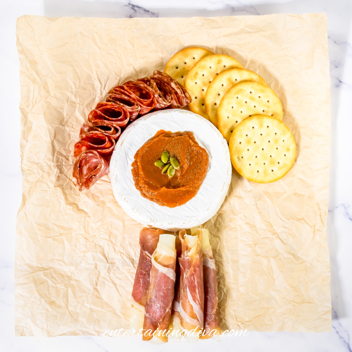 A fall charcuterie board with brie, pumpkin butter, salami, crackers and prosciutto wrapped mozzarella