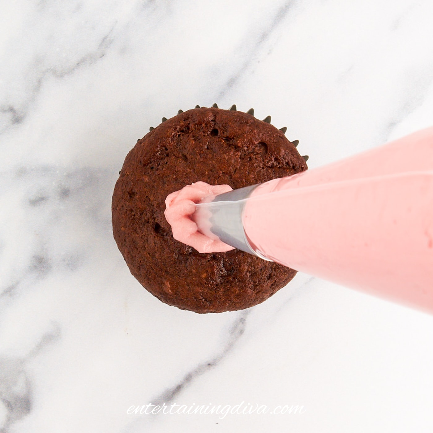 Pink buttercream frosting being piped onto a chocolate cupcake.