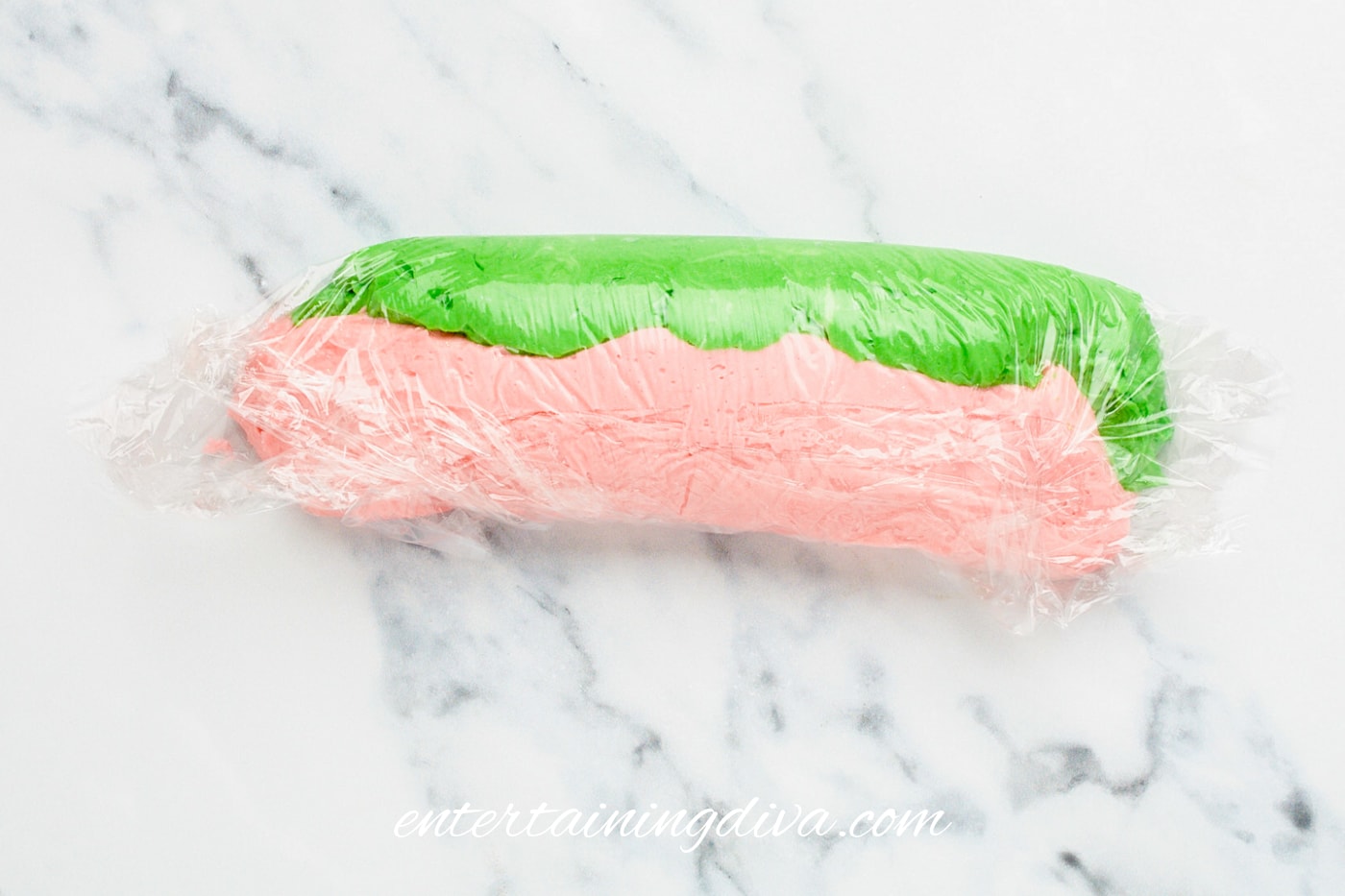 A roll of pink and green buttercream frosting in plastic wrap.