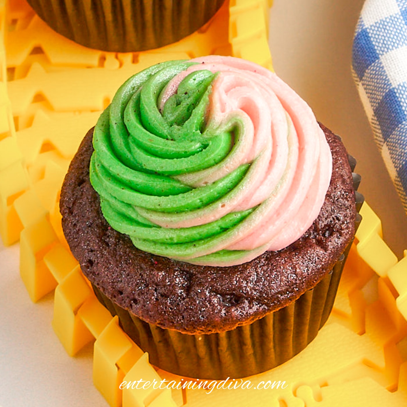 Pink and green swirled frosting on top of a chocolate cupcake