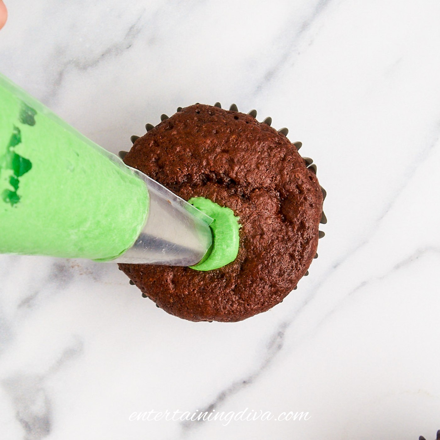 Piping green buttercream frosting onto a chocolate cupcake