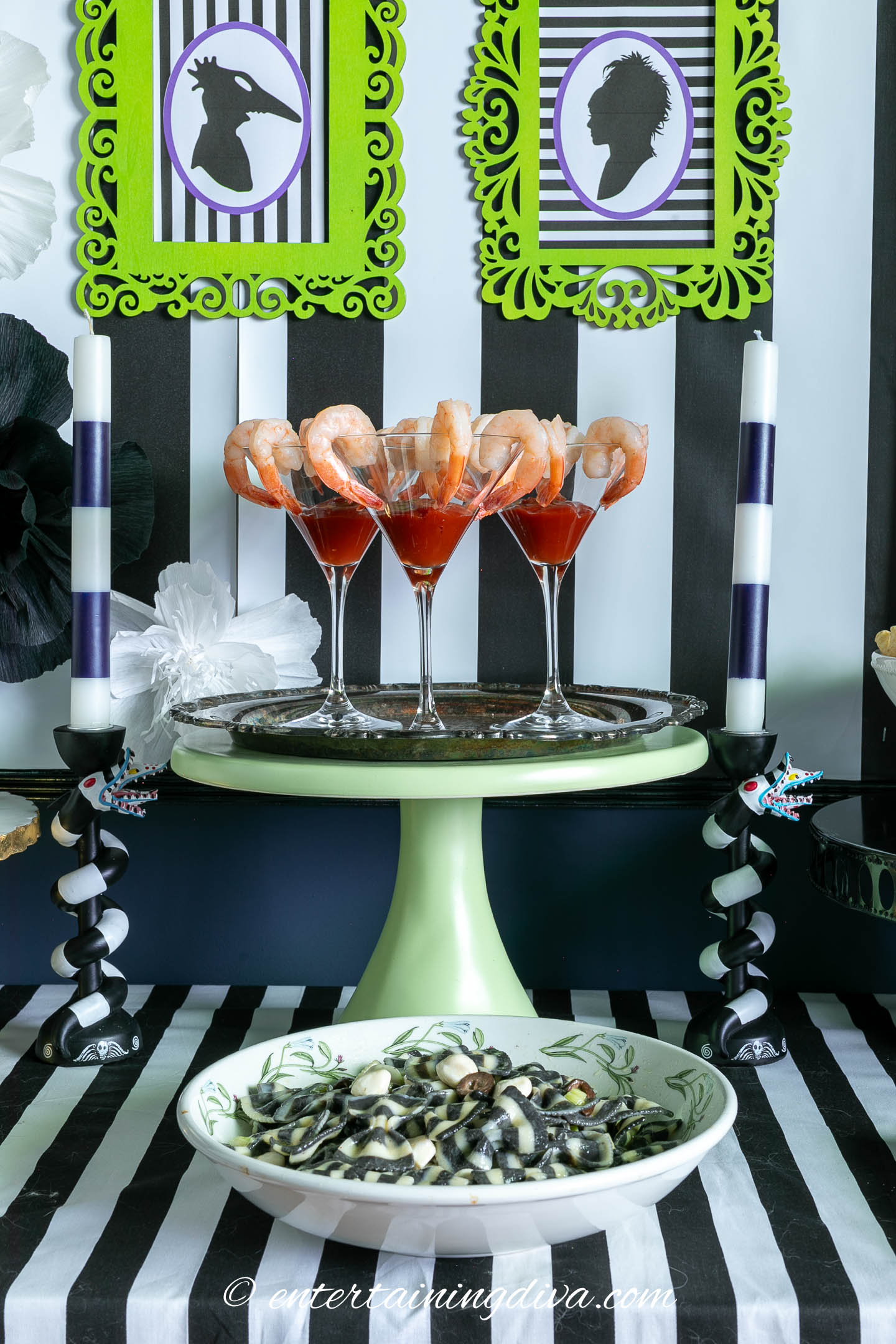 Shrimp cocktails on a cake tray behind a bowl of black and white striped bow tie pasta salad on a Beetlejuice buffet table