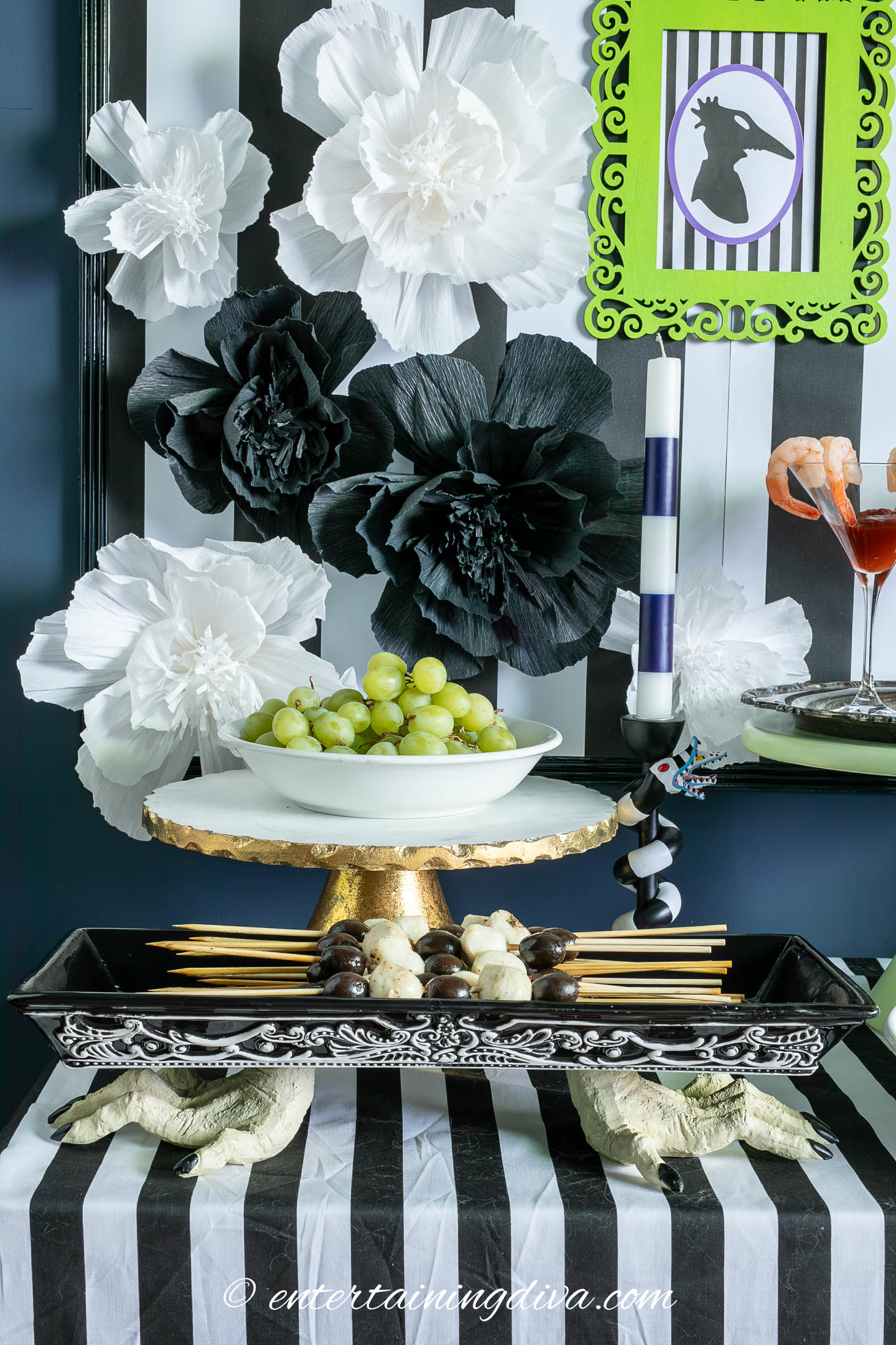 Black and white olive and mozzarella skewers in a black and white skeleton hand tray in front of green grapes and a black and white background