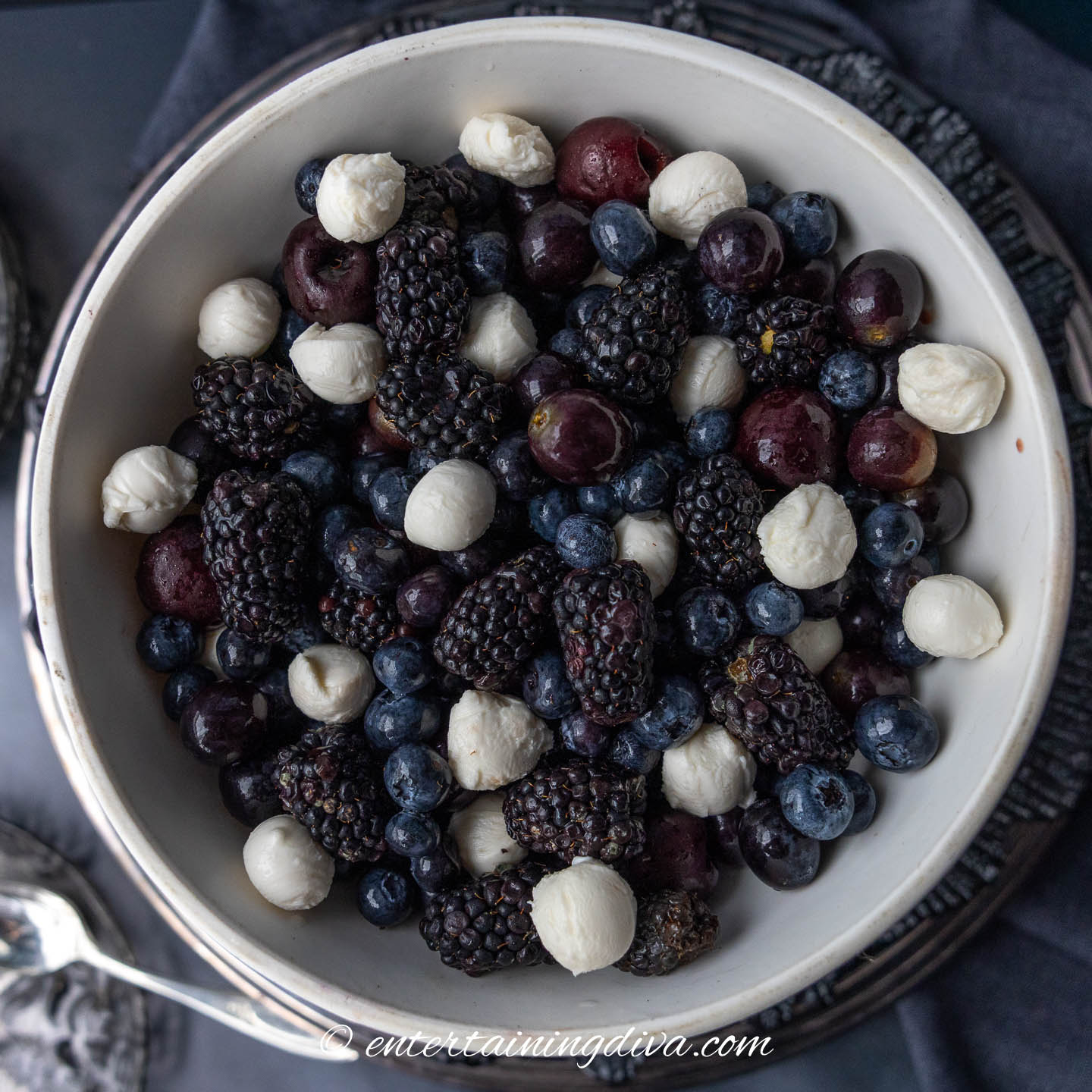 a dark fruit salad with white mozzarella pearls in a white bowl