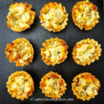 Nine phyllo pastry cups filled with a diced potato and cheese mixture, arranged in a grid on a black slate surface.