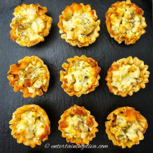 Nine phyllo pastry cups filled with a diced potato and cheese mixture, arranged in a grid on a black slate surface.
