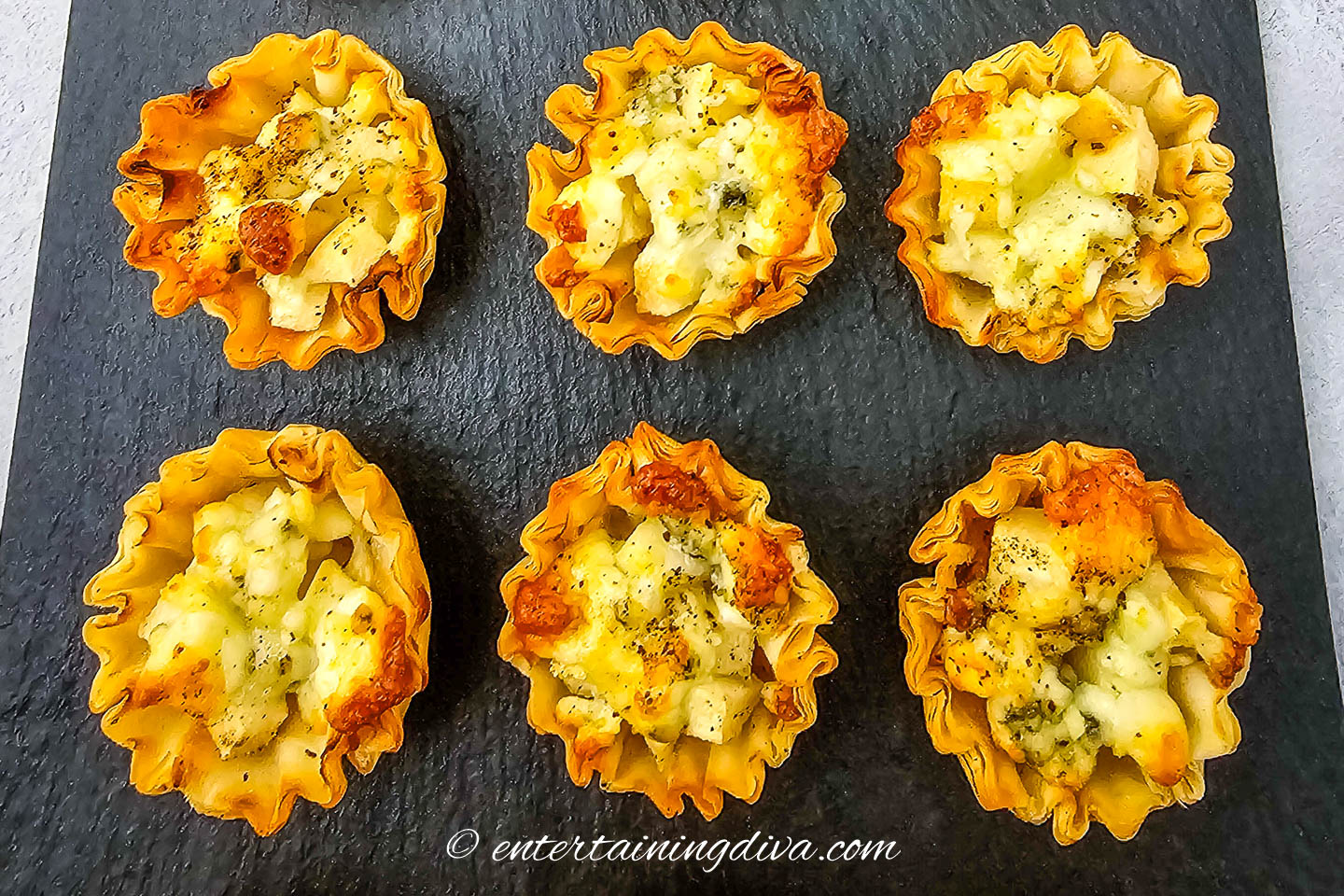 Six blue cheese and pear tartlets on a black serving tray