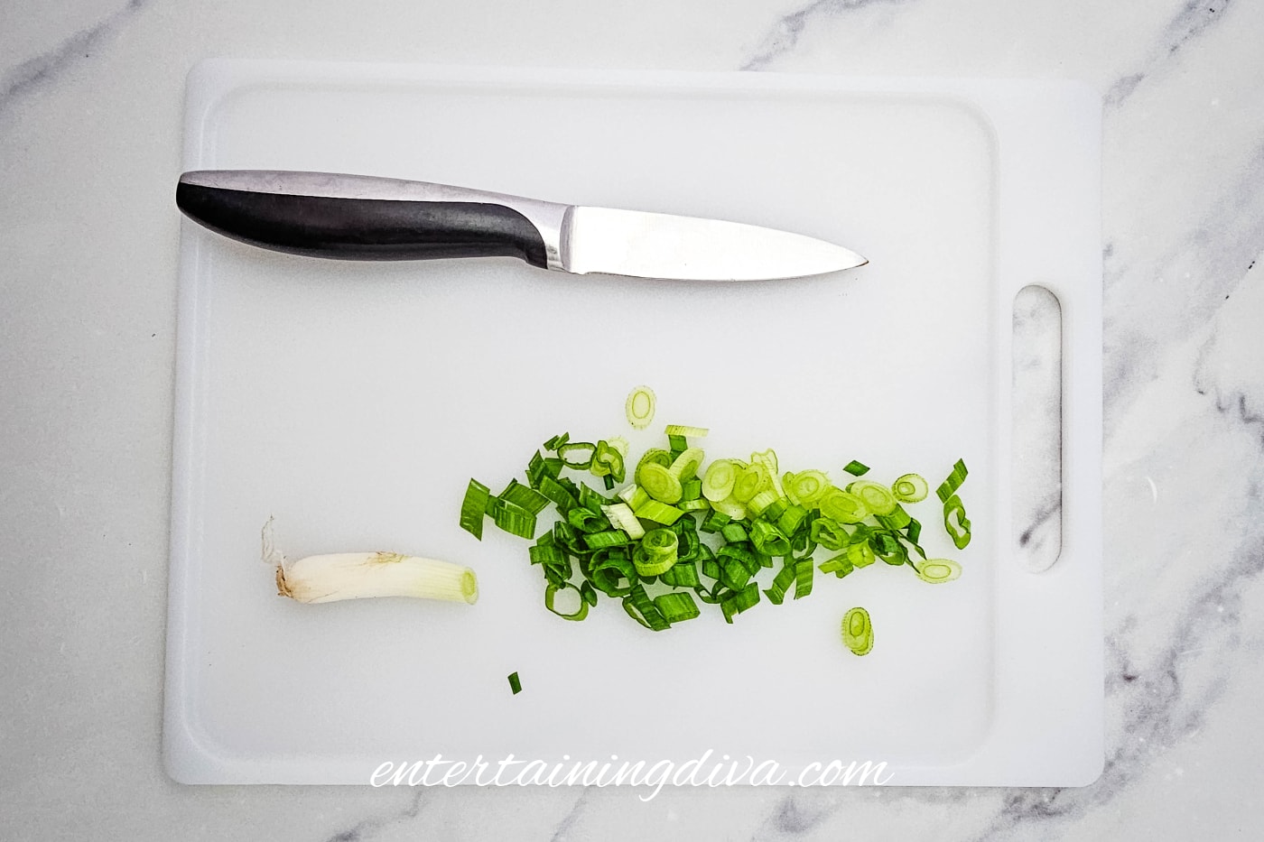 a cutting board with chopped green onions and a paring knife