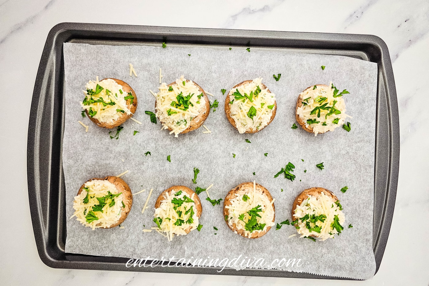 crab-stuffed mushrooms on a baking sheet with parmesan cheese and herbs sprinkled on top