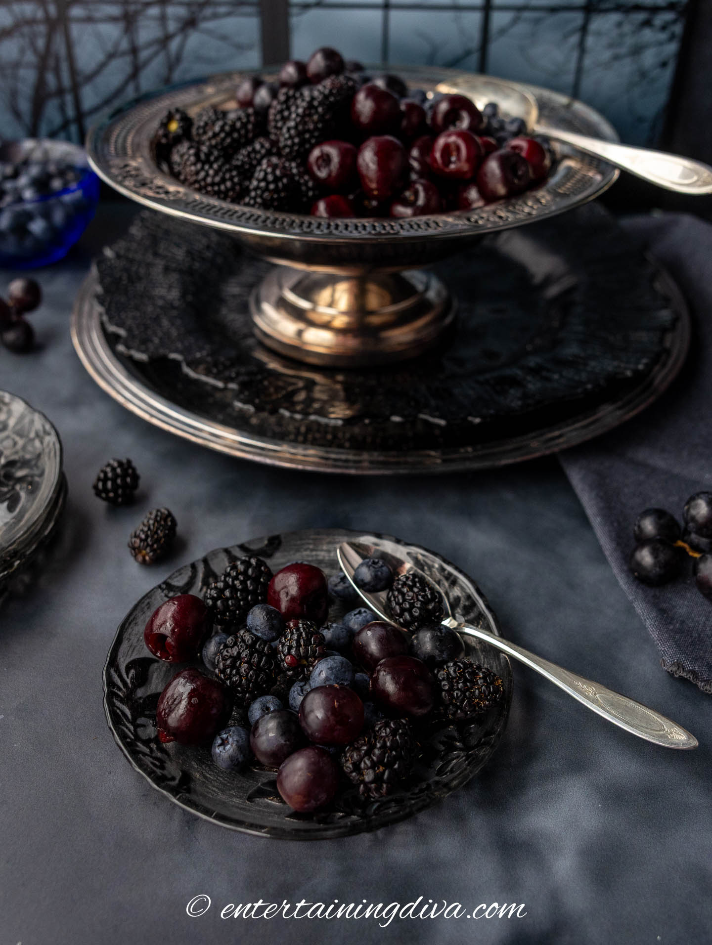 A plate of dark Halloween fruit salad in front of a serving bowl with more of the dark fruit salad.