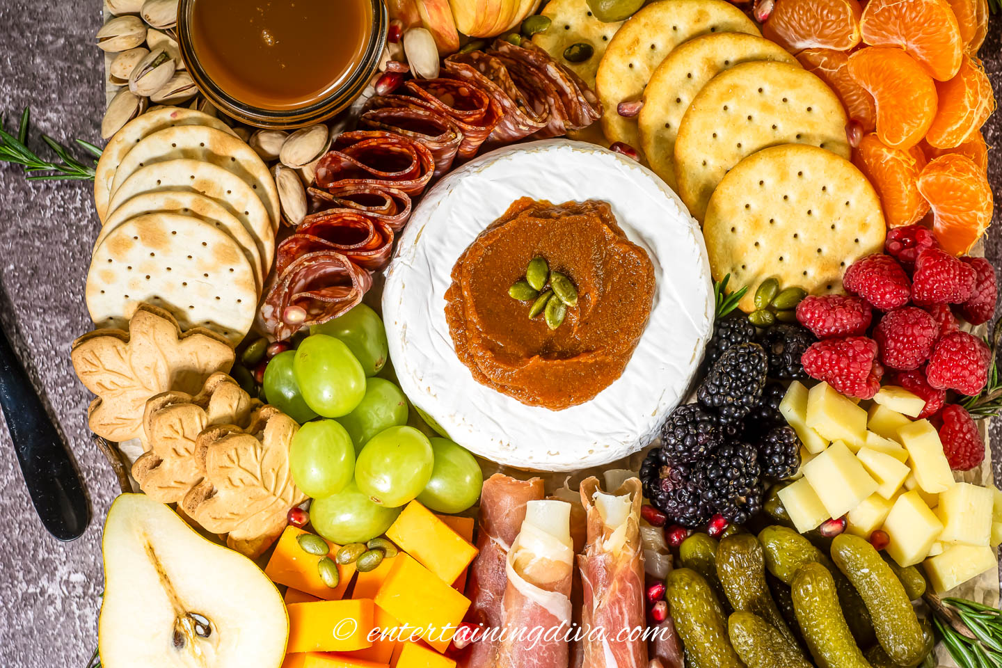 Overhead of a fall charcuterie board with crackers, pears, cheddar, brie, grapes, berries, oranges, pickles and prosciutto wrapped mozzarella