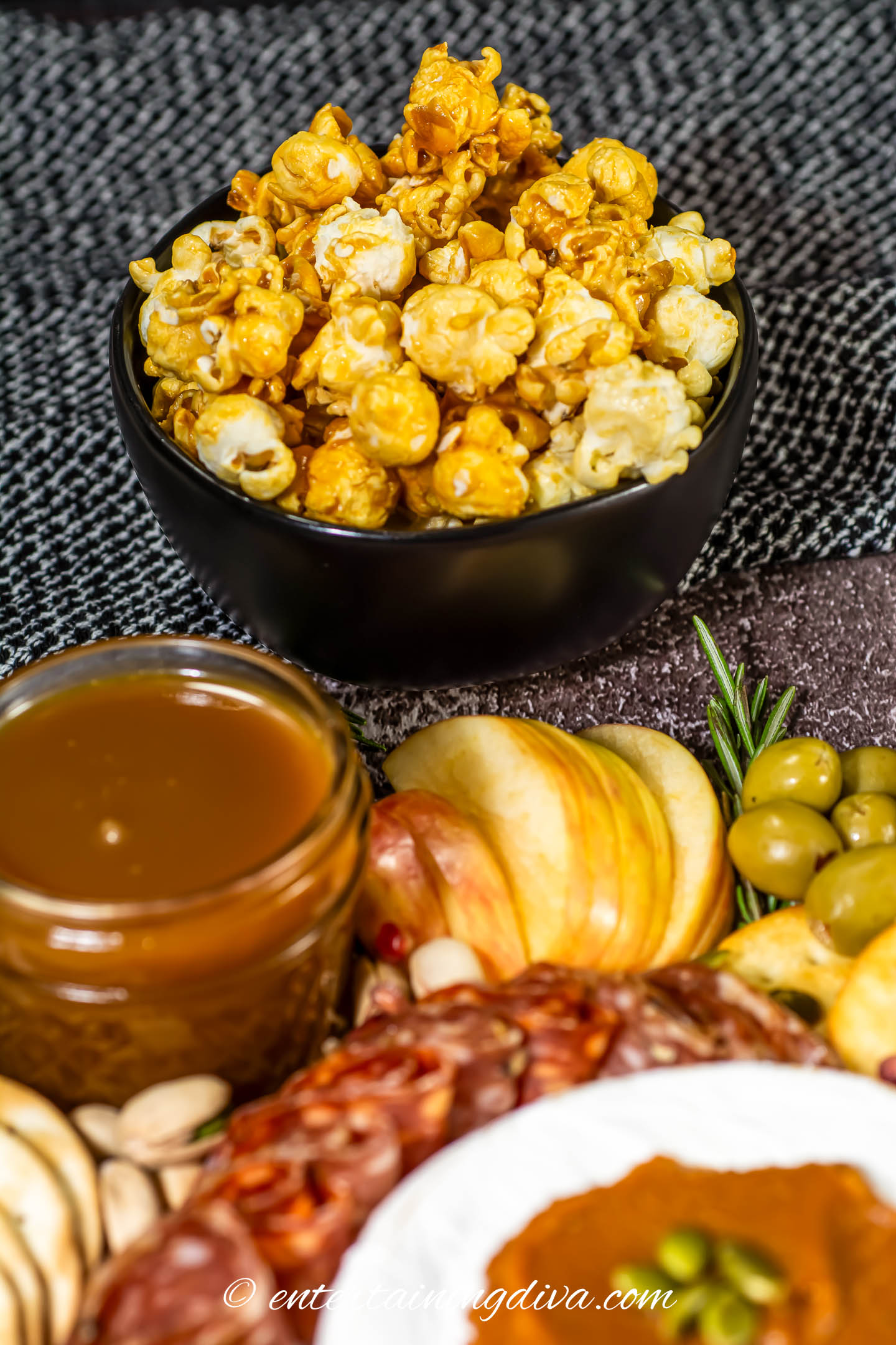 A bowl of caramel popcorn being served with a fall charcuterie board