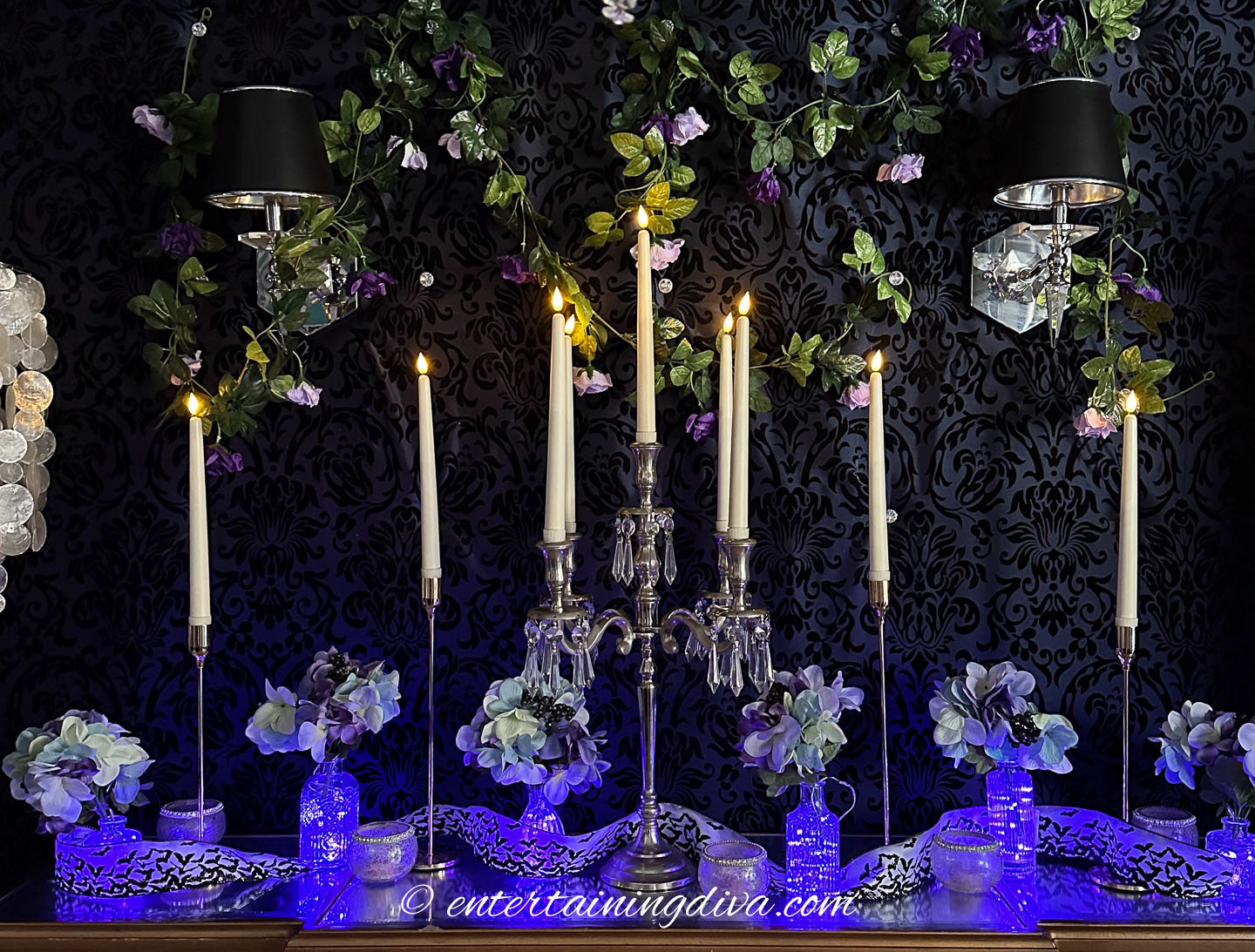 Flameless taper candles on a buffet with vases filled with fairy lights and faux flowers
