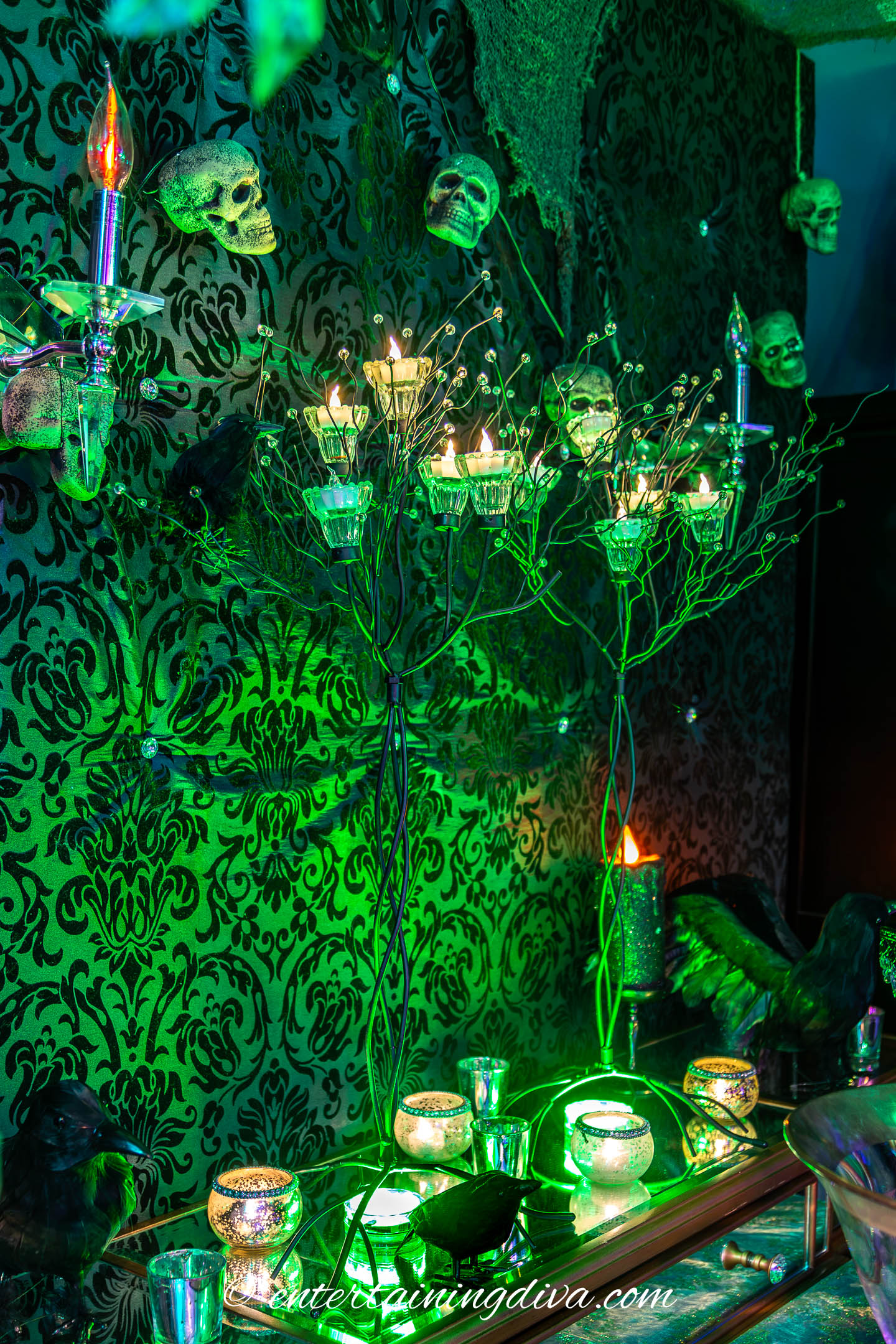 Green uplights on a Halloween buffet under candle trees with crows, skulls and creepy cloth
