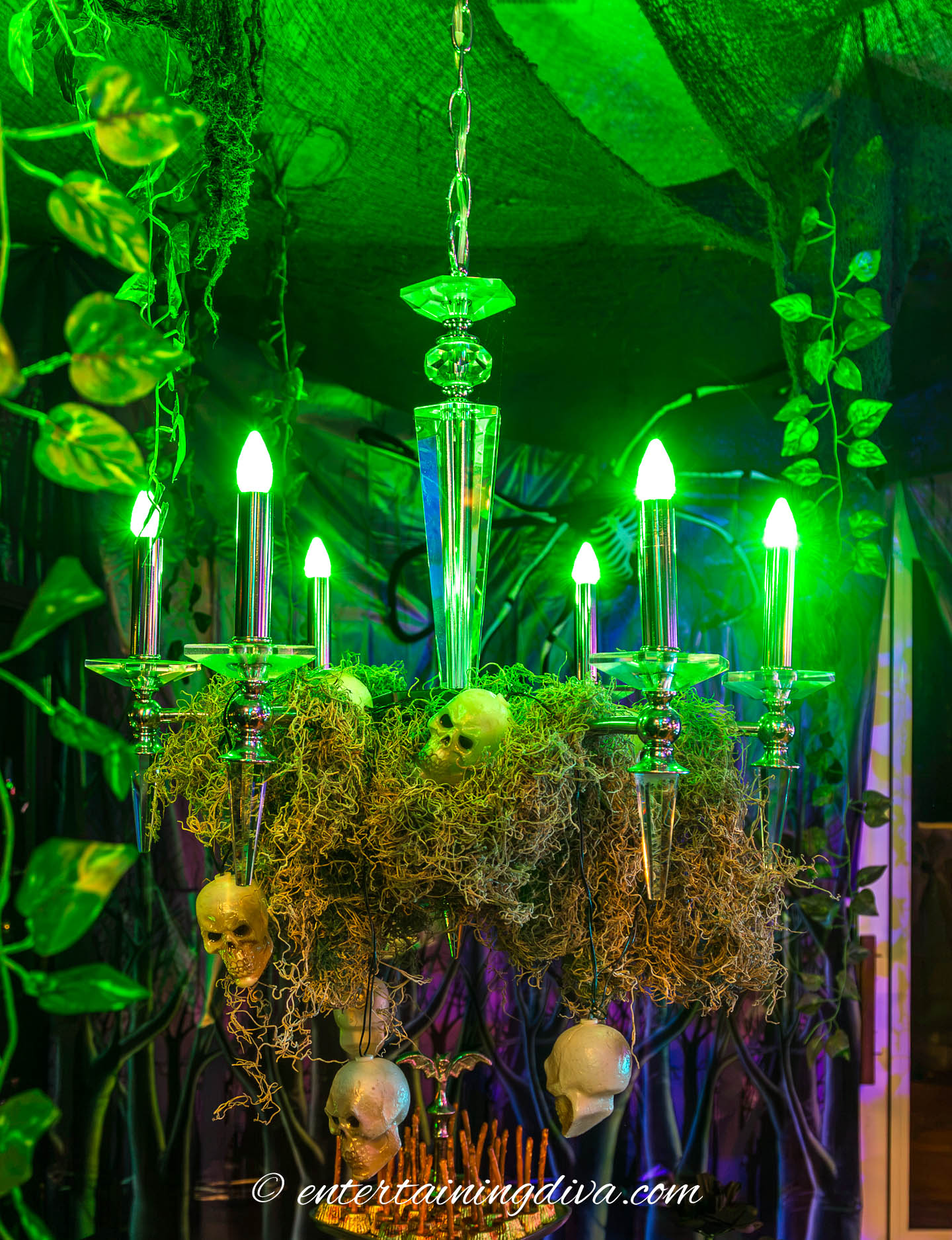 Chandelier with green lightbulbs, moss and small skeleton heads in a haunted house