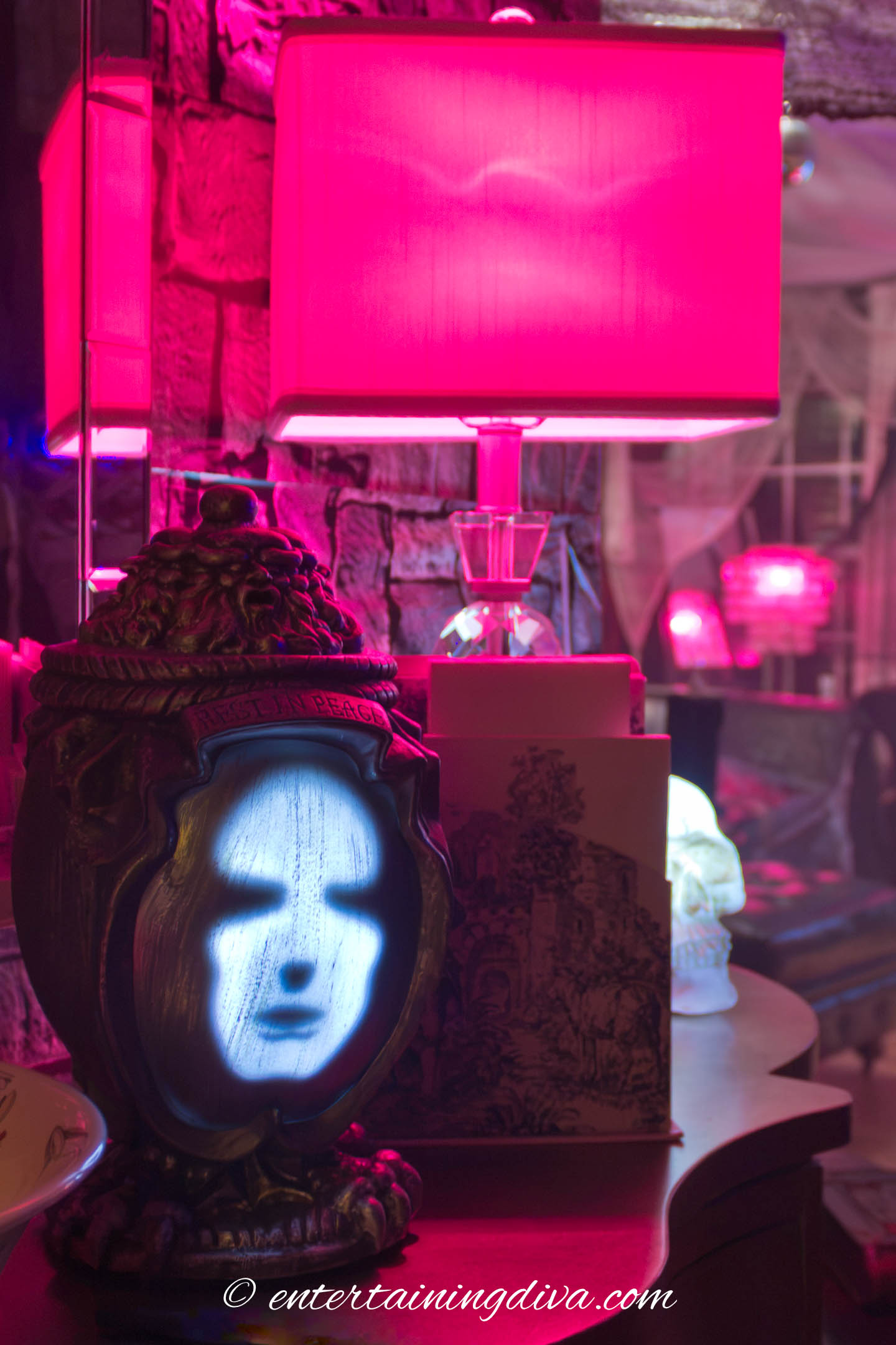 A lamp with a red lightbulb behind an urn prop with a light-up face on the front