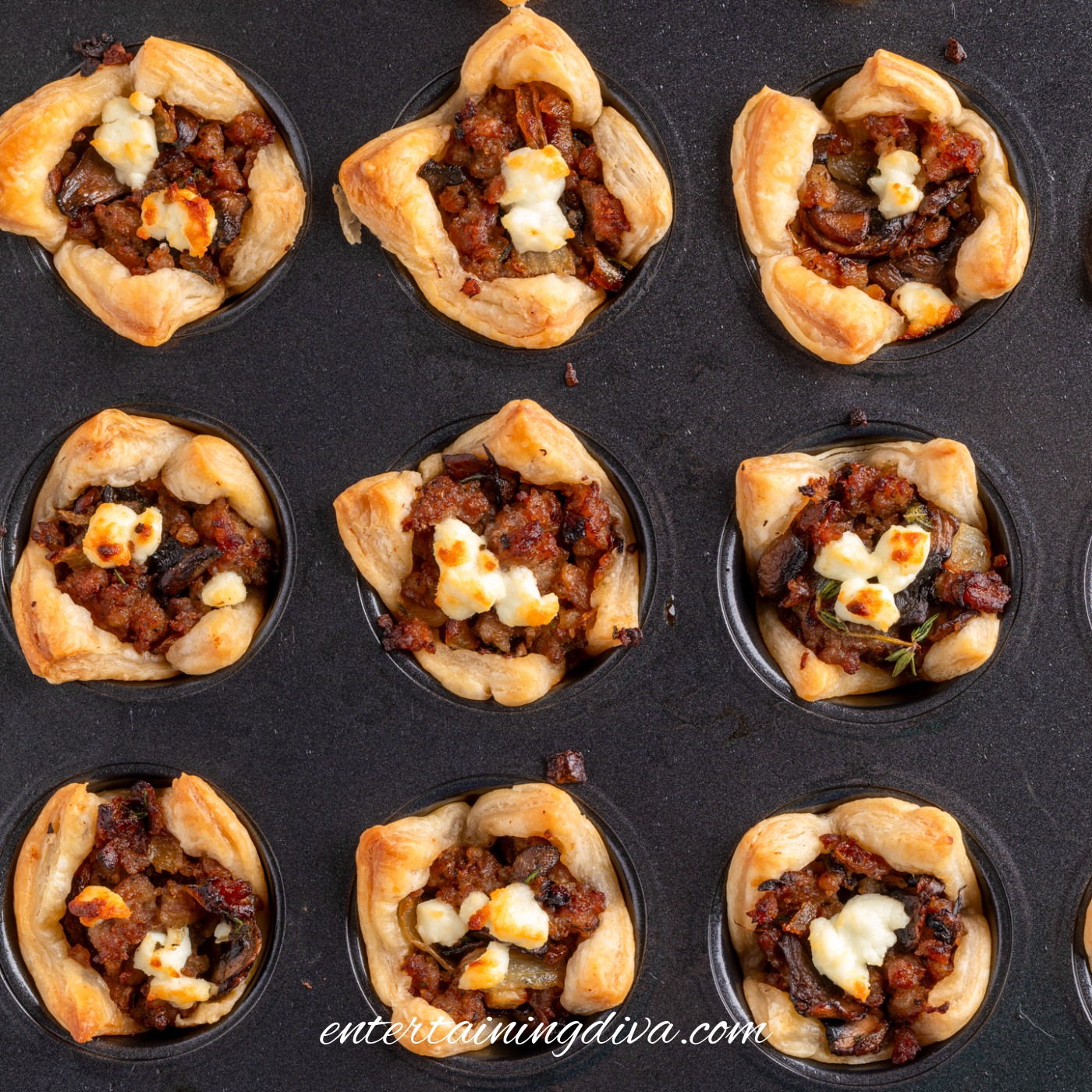 Mini puff pastry tarts filled with a savory sausage, mushroom and goat cheese mixture, in a mini muffin tin after baking.