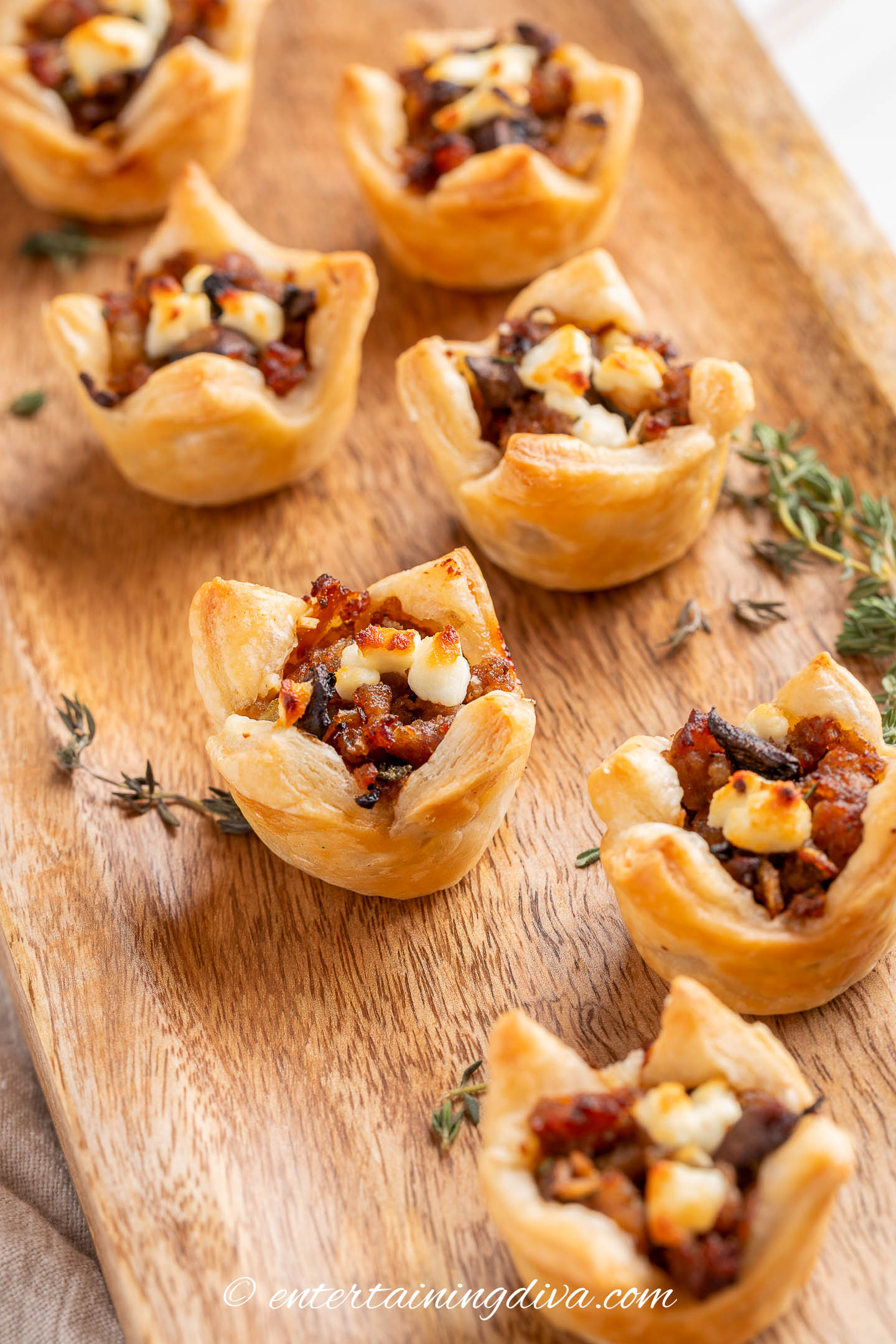 Two lines of mushroom sausage puff pastry bites on a wooden serving tray