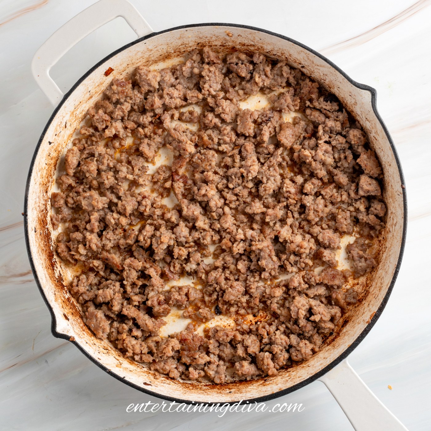 Cooked ground sausage in a white skillet with browned bits and some oil visible in the pan.