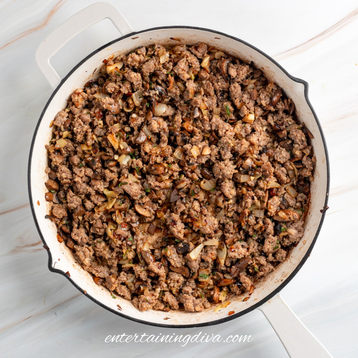Cooked ground pork sausage with onions, mushrooms, and herbs in a white skillet.