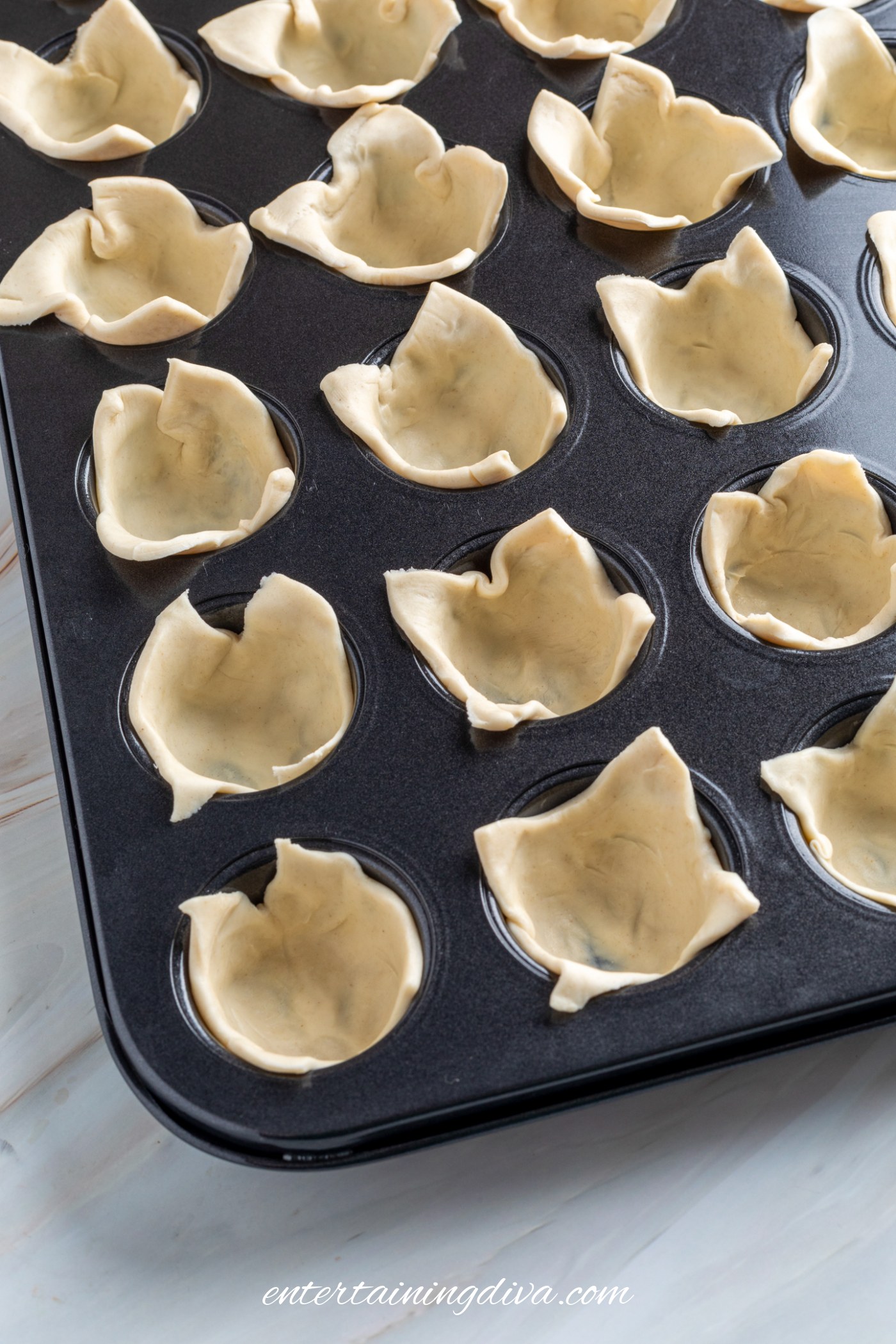 A mini muffin tin filled with unbaked puff pastry dough pressed into each cup, ready to be filled or baked.