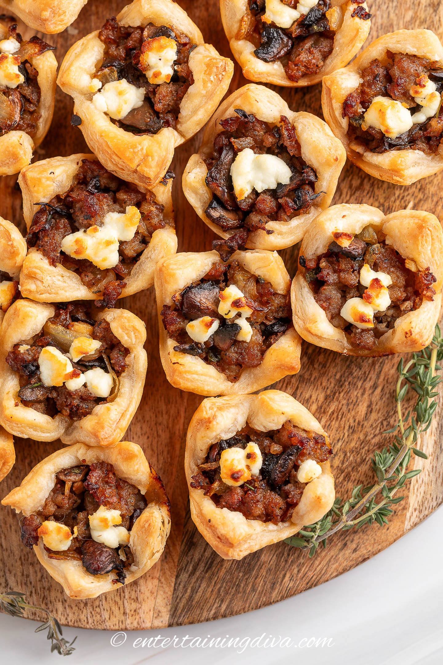 overhead view of a group of mushroom sausage puff pastry bites on a wooden serving tray