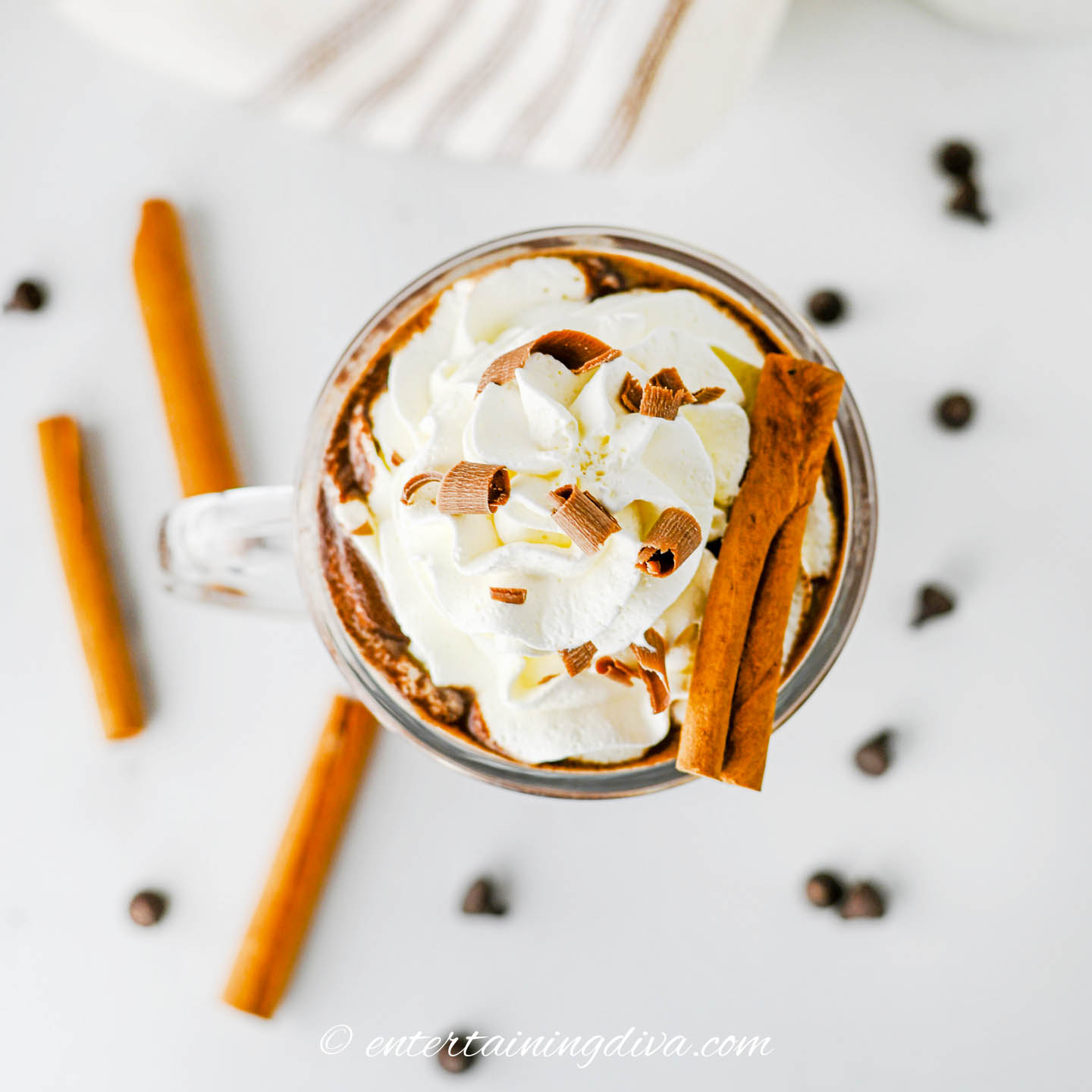 overhead view of whipped cream, chocolate shavings and a cinnamon stick on top of a glass of rumchata hot chocolate