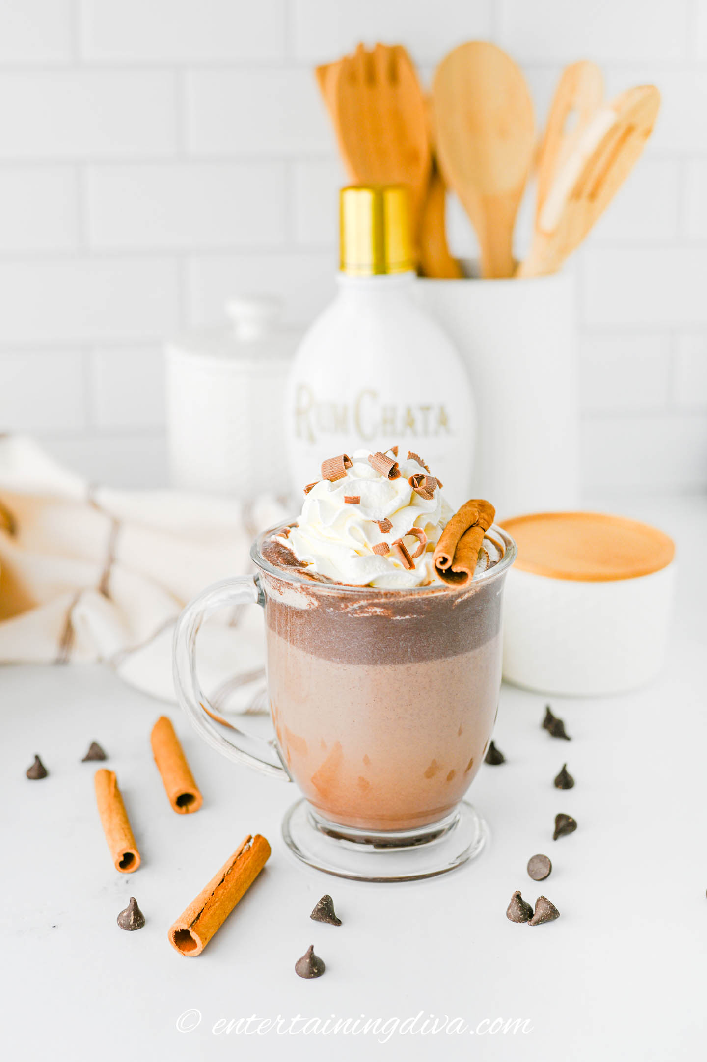 rumchata hot chocolate in a glass mug with whipped cream on top and a bottle of RumChata in the background
