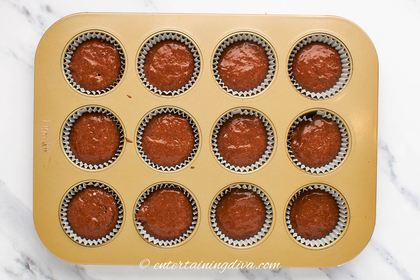 A 12-cup muffin tin filled with chocolate cupcake mix before baking