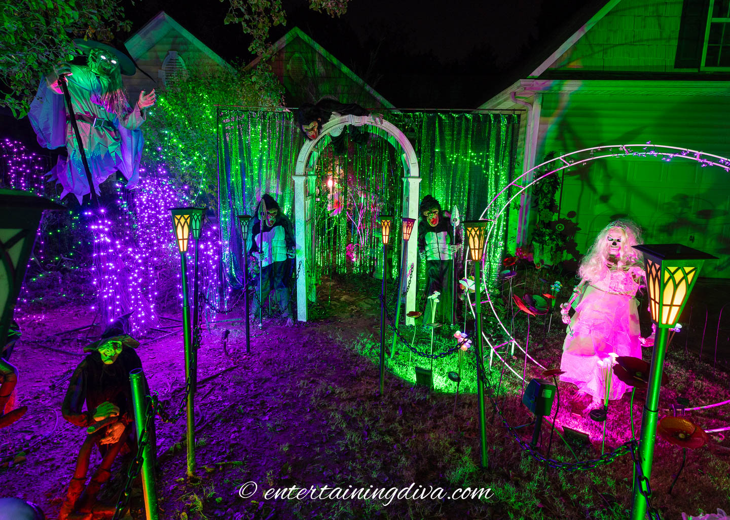A front yard with Wicked Themed Outdoor decorations including an Elphaba witch, flying monkeys, Glinda and green lighting