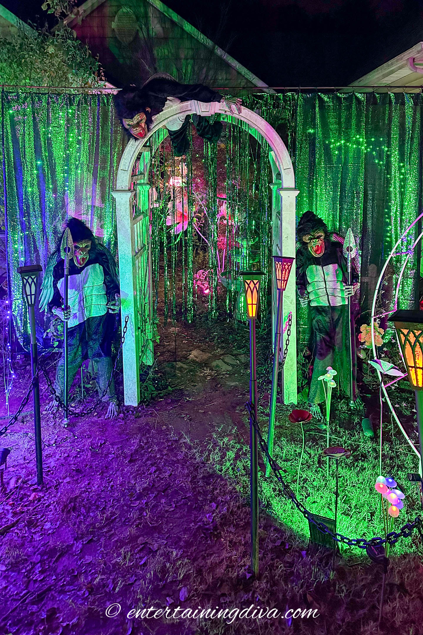 Three flying monkeys around an arbor in a Wicked themed Halloween front yard display at night