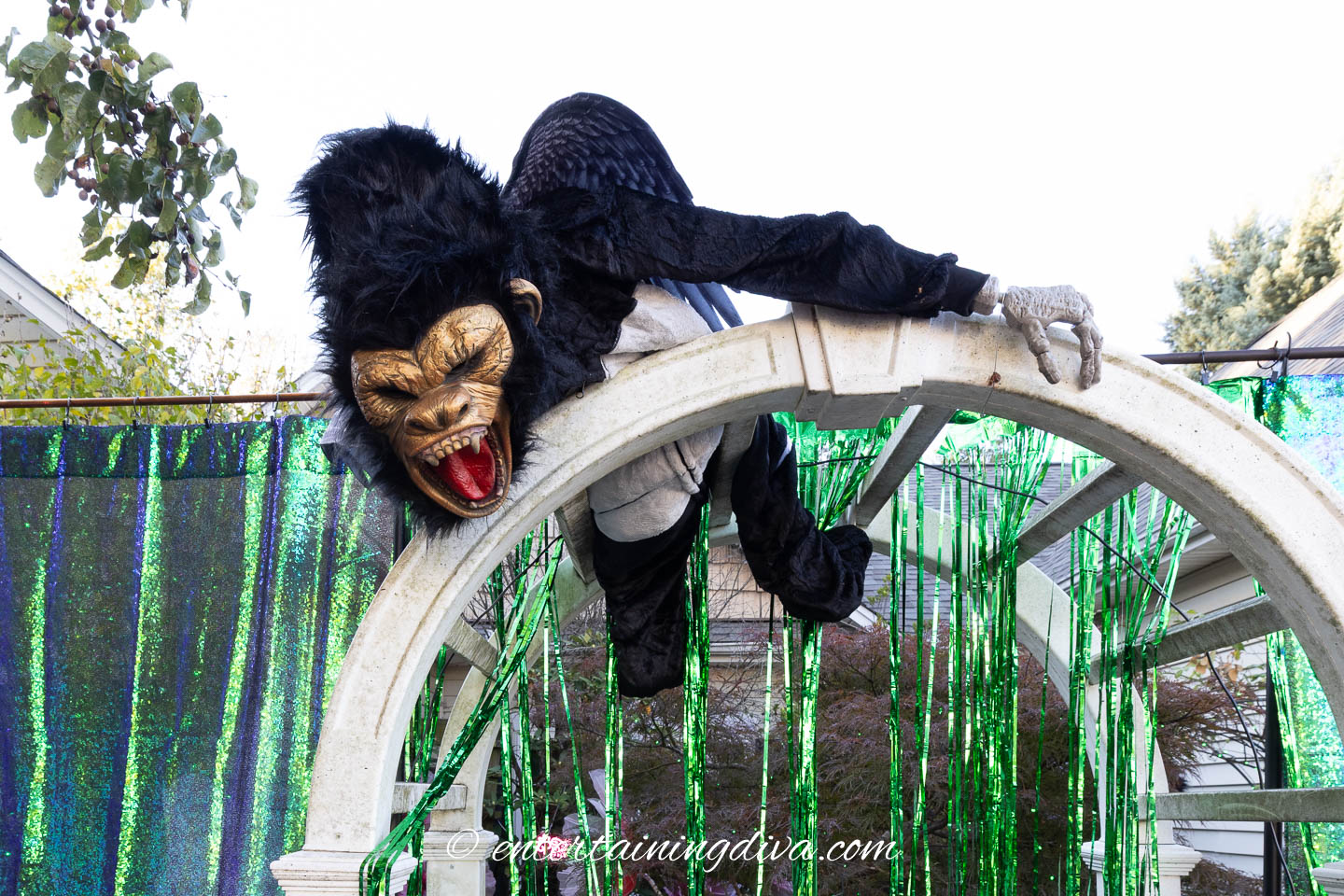 A skeleton dressed like a flying monkey positioned on the top of an arbor in a Halloween front yard