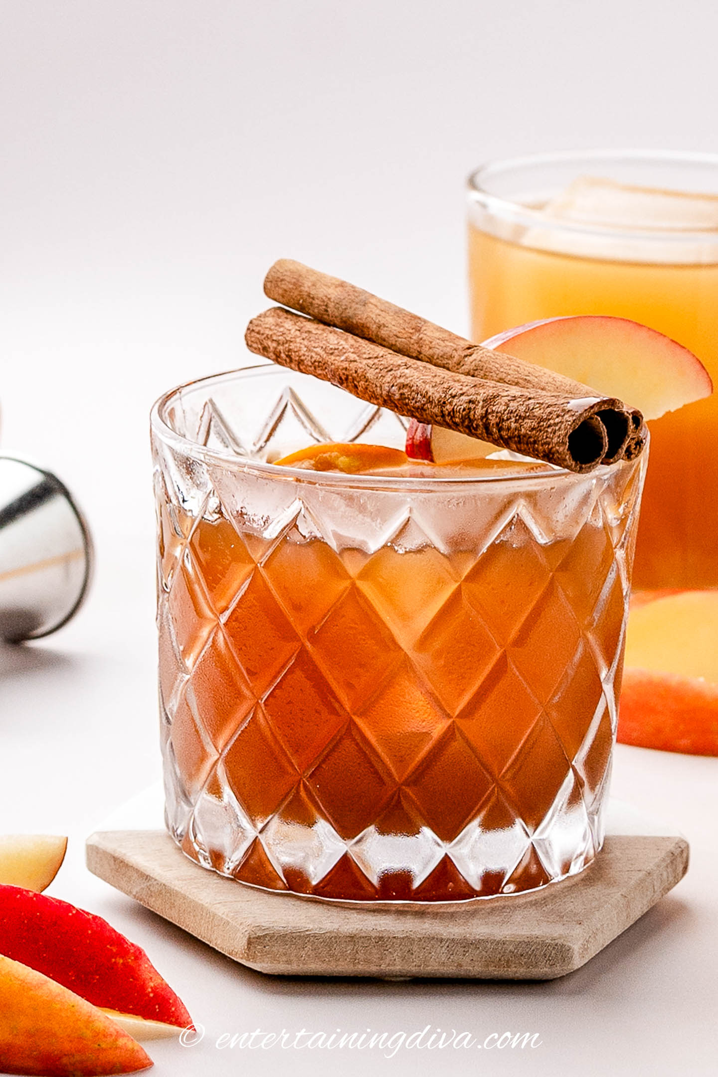 An apple butter old fashioned garnished with cinnamon sticks and an apple wedge on the rim