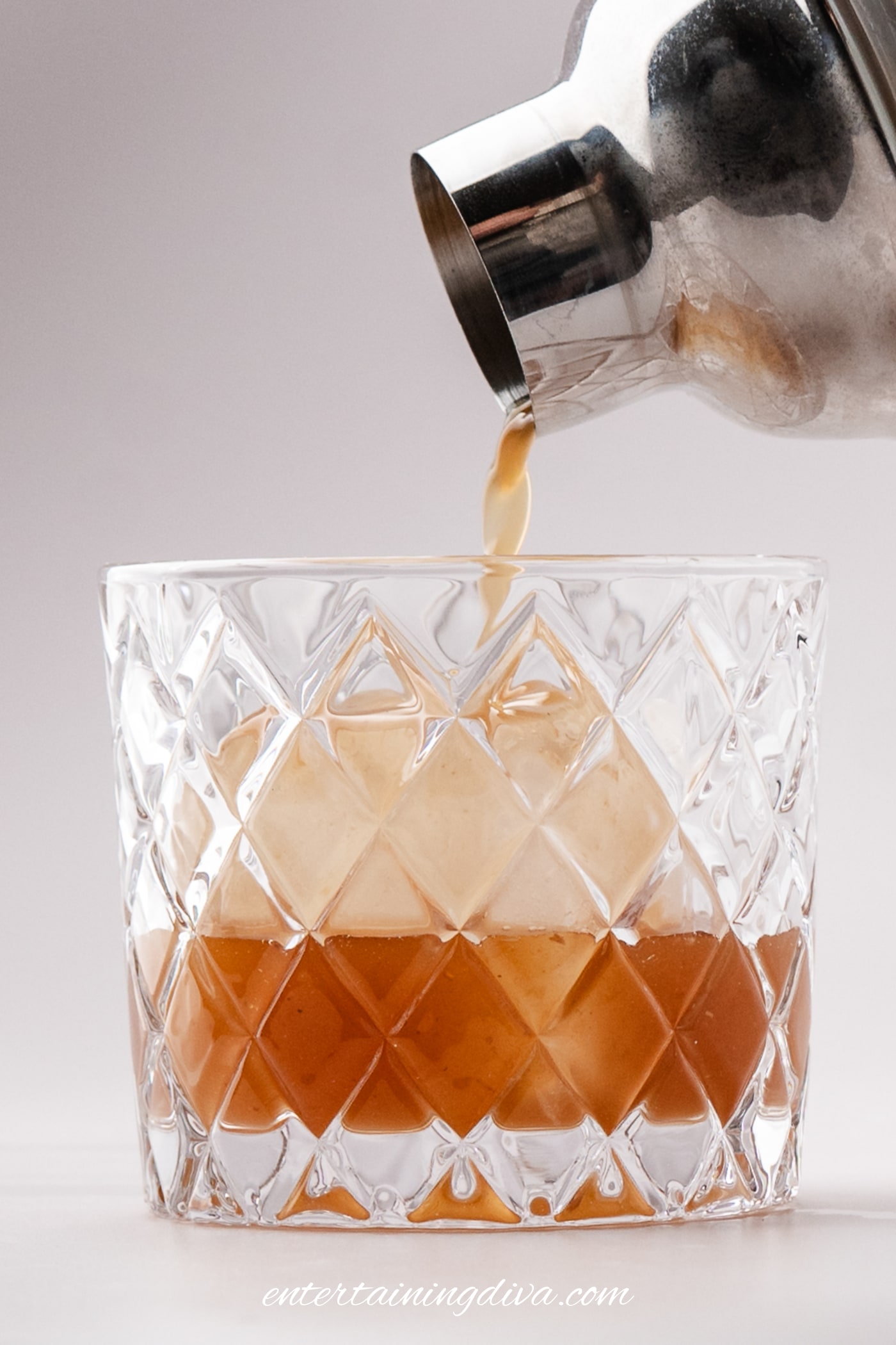 Apple butter old fashioned being poured over a large ice cube in a glass