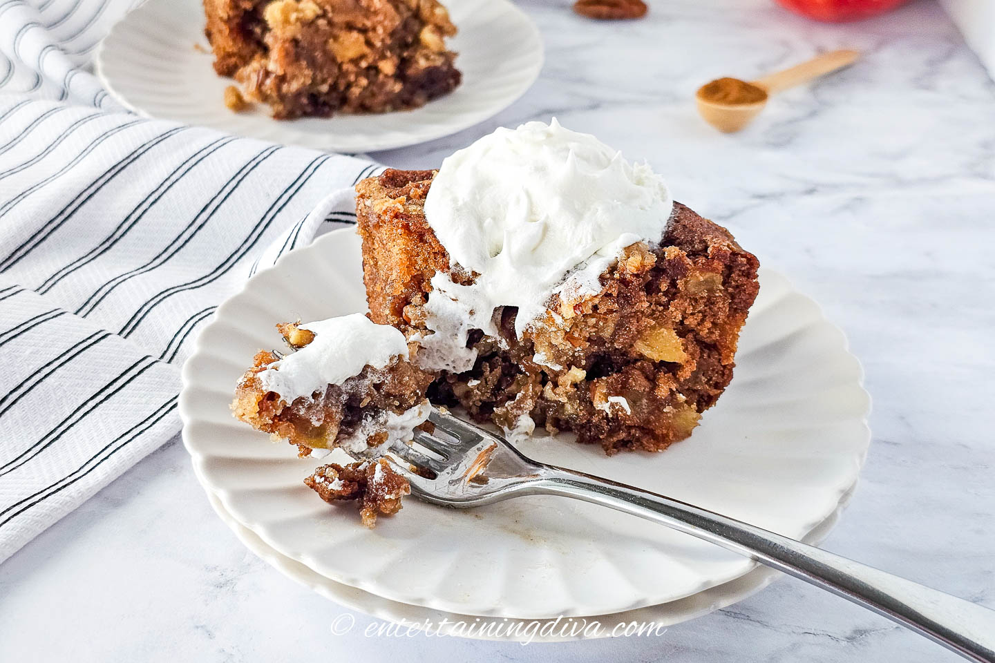 Apple crumb cake with whipped cream and a fork on a white plate