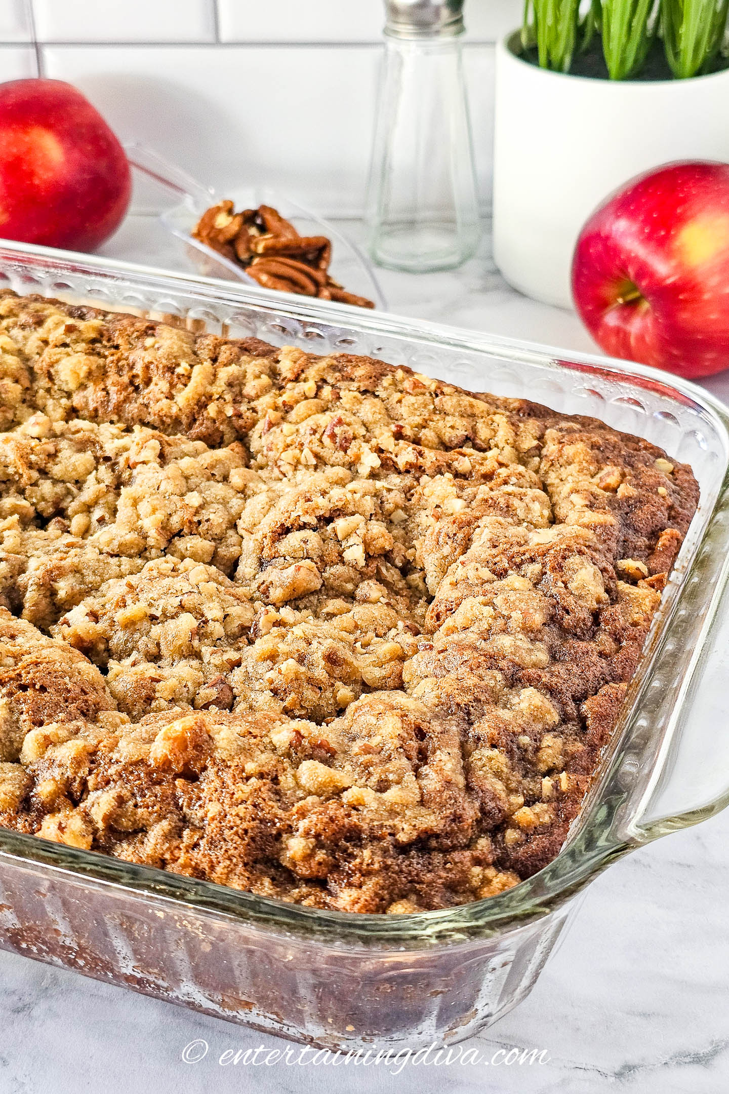 Apple crumb sheet cake in a baking pan with apples and walnuts in the background.