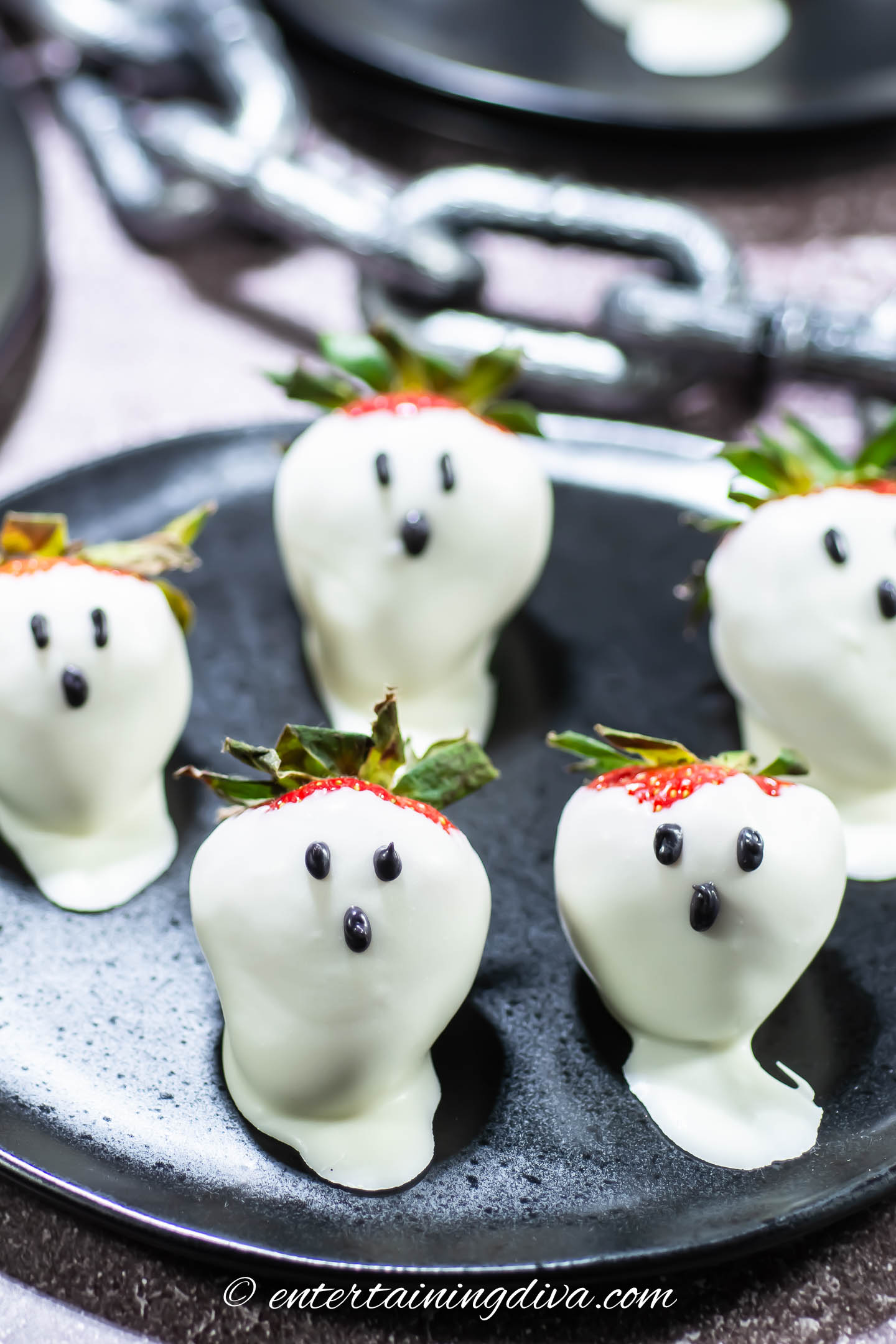 A group of ghost strawberries on a Halloween table with a black chain in the background