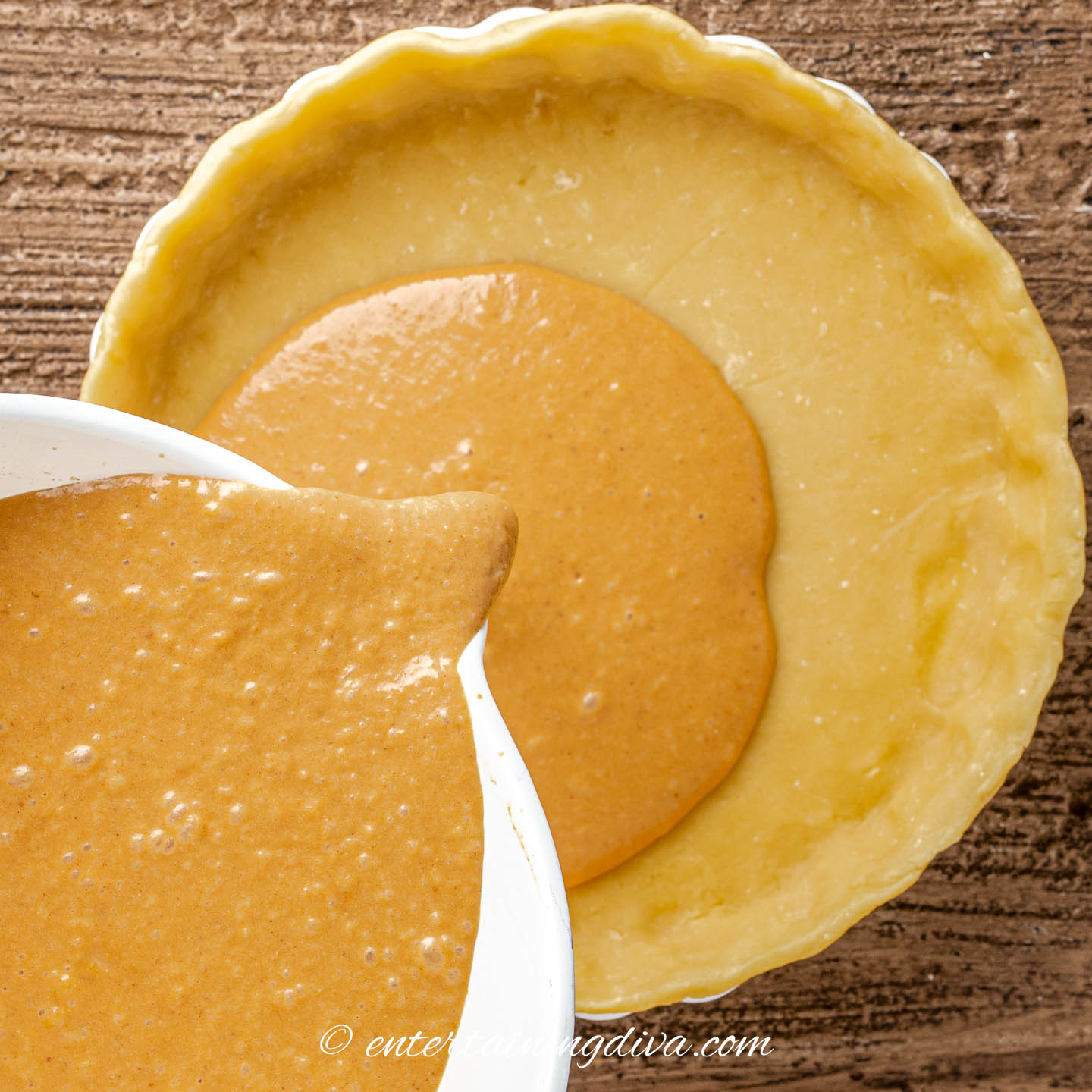 pumpkin pie filling being poured into a pie shell