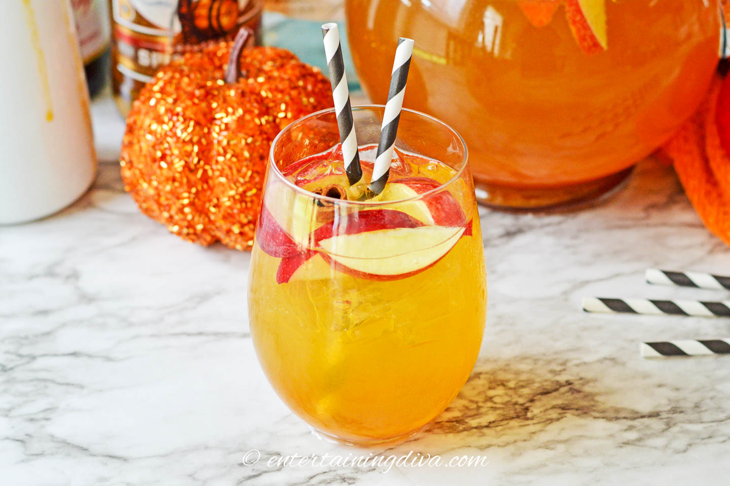 pumpkin sangria in a glass on a countertop in front of a pitcher and a pumpkin