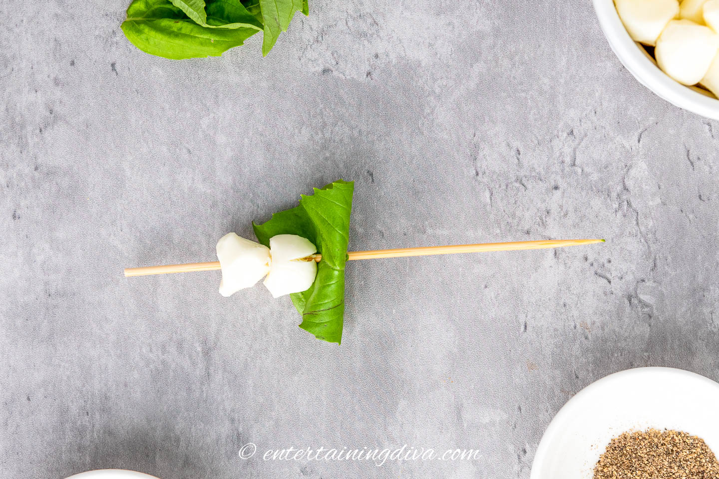 2 mozzarella pearls and a folded basil leaf on a skewer