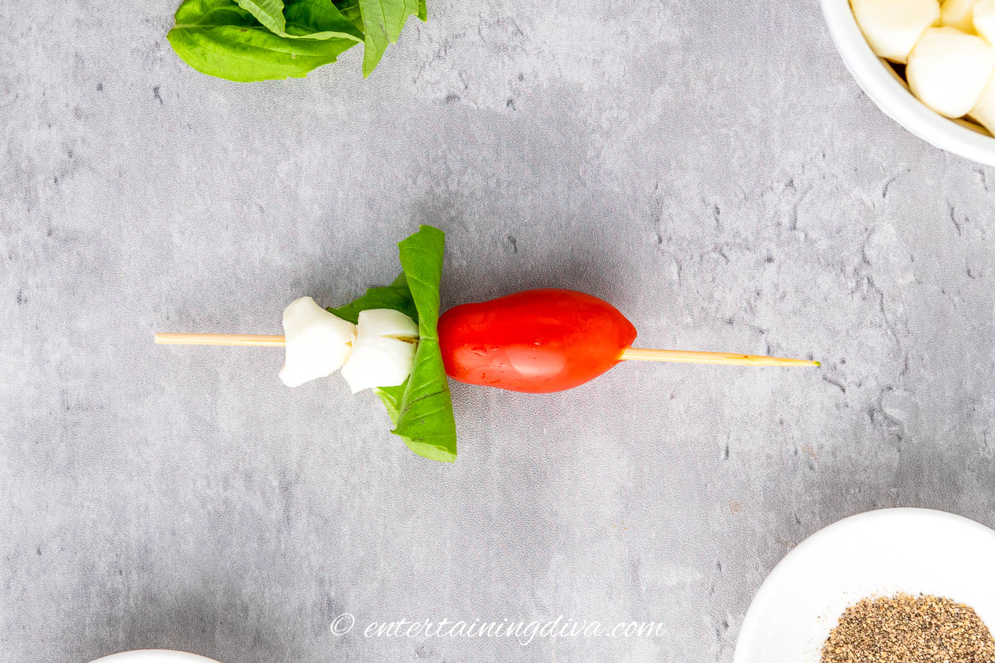 2 mozzarella pearls, a folded basil leaf and a grape tomato on a skewer