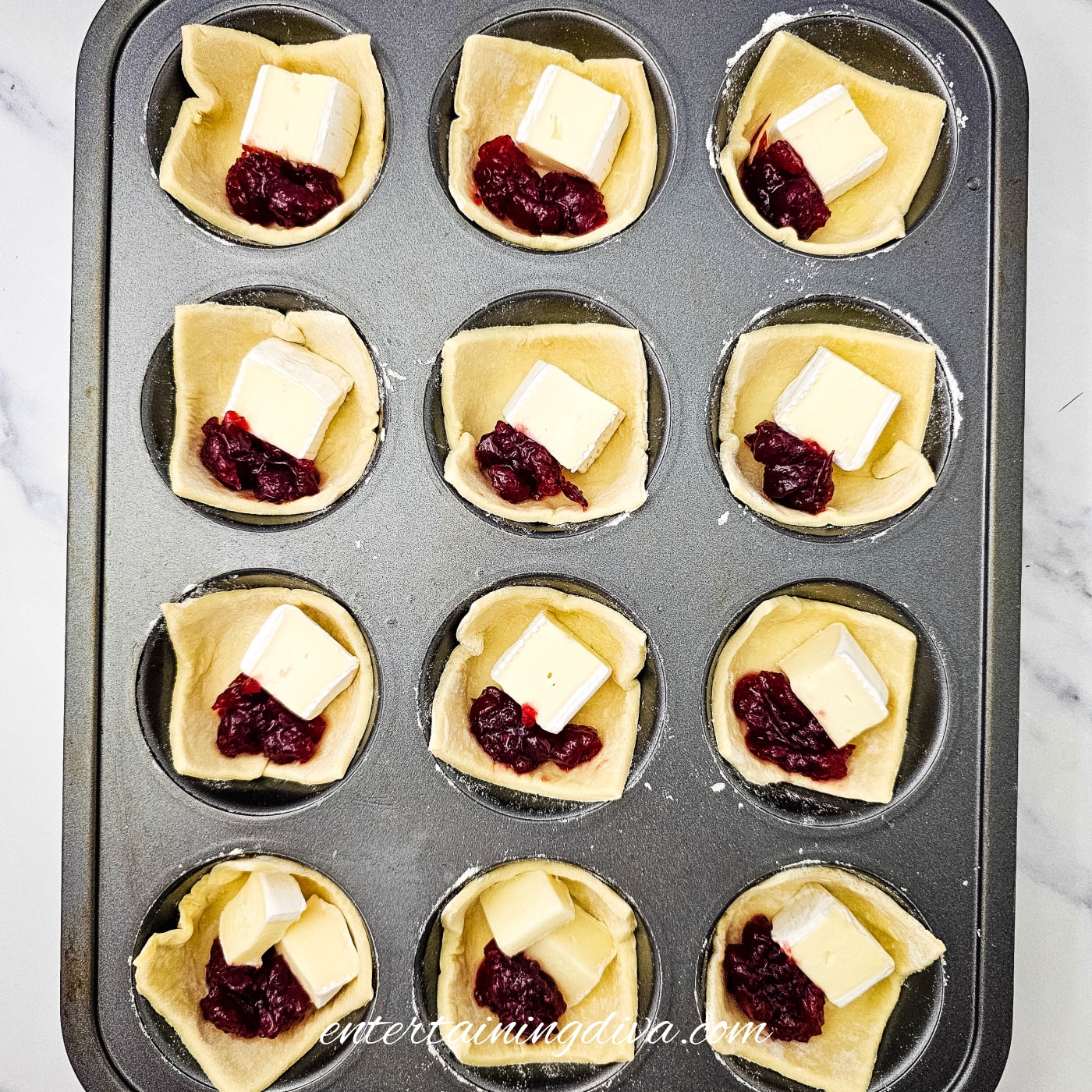 Puff pastry cups filled with Brie and spoonfuls of cranberry sauce before baking.