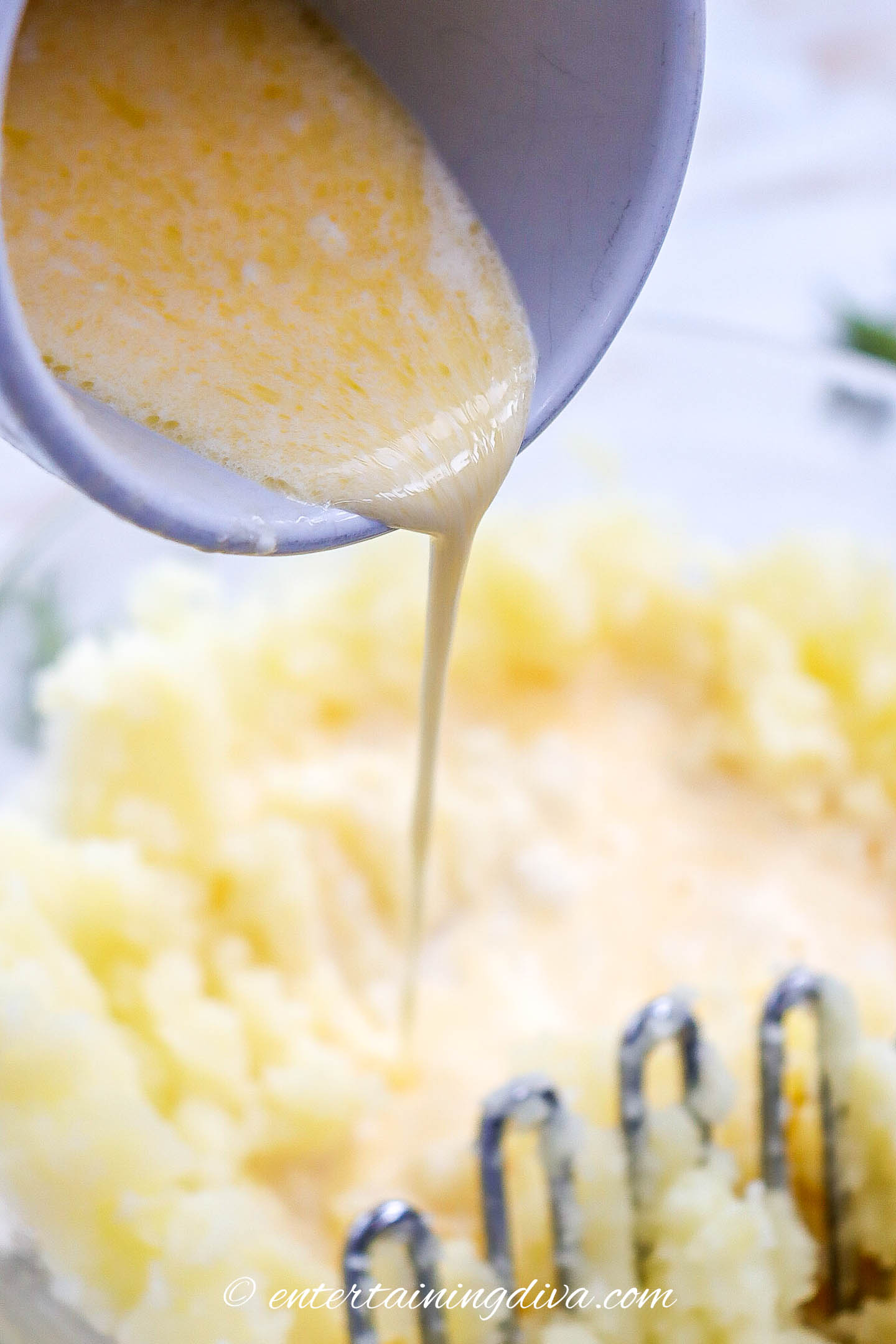 garlic butter mixture being poured into mashed potatoes