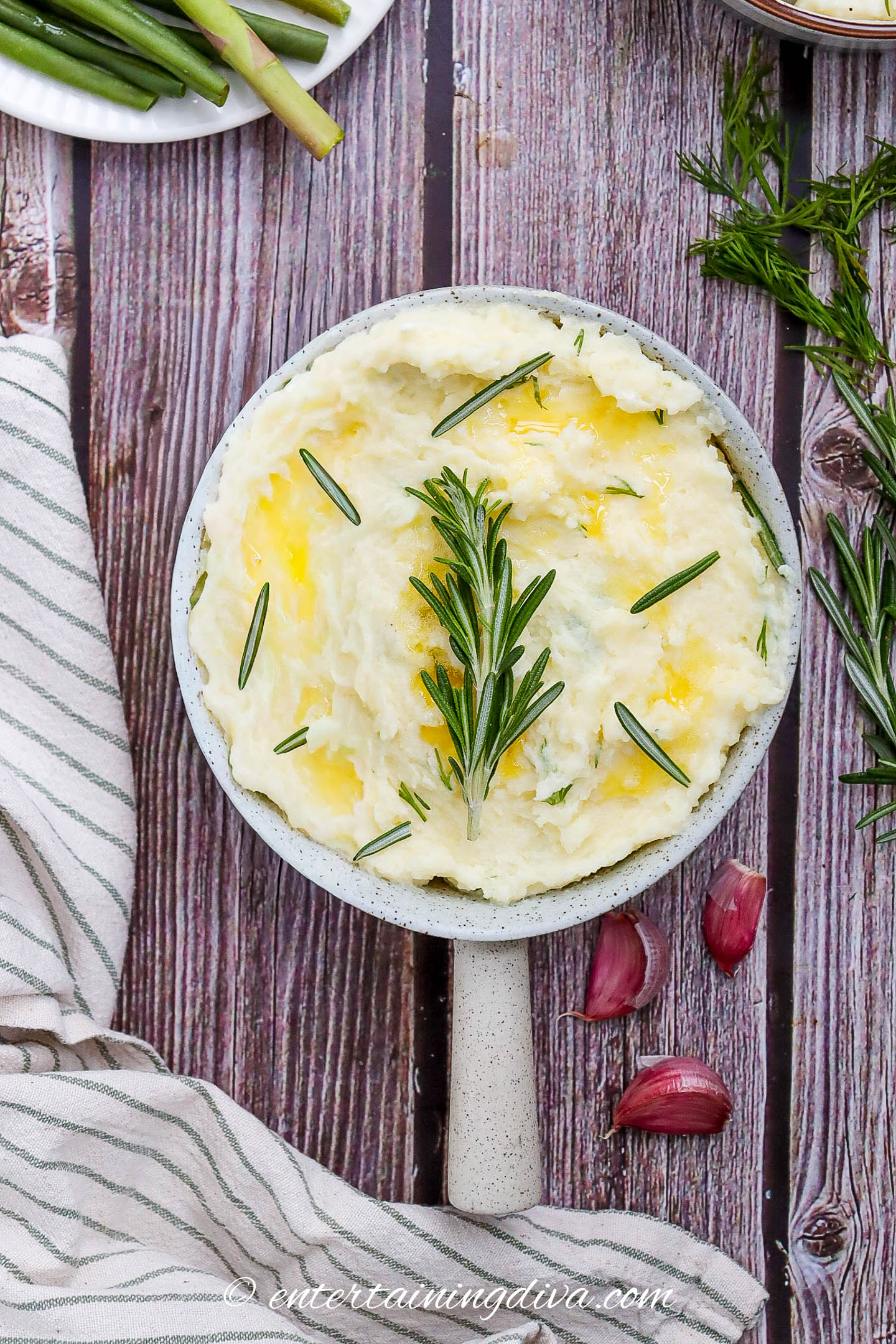 overhead view of garlic mashed potatoes in a serving bowl garnished with rosemary