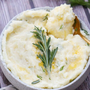 close up of garlic mashed potatoes with a sprig of rosemary as garnish