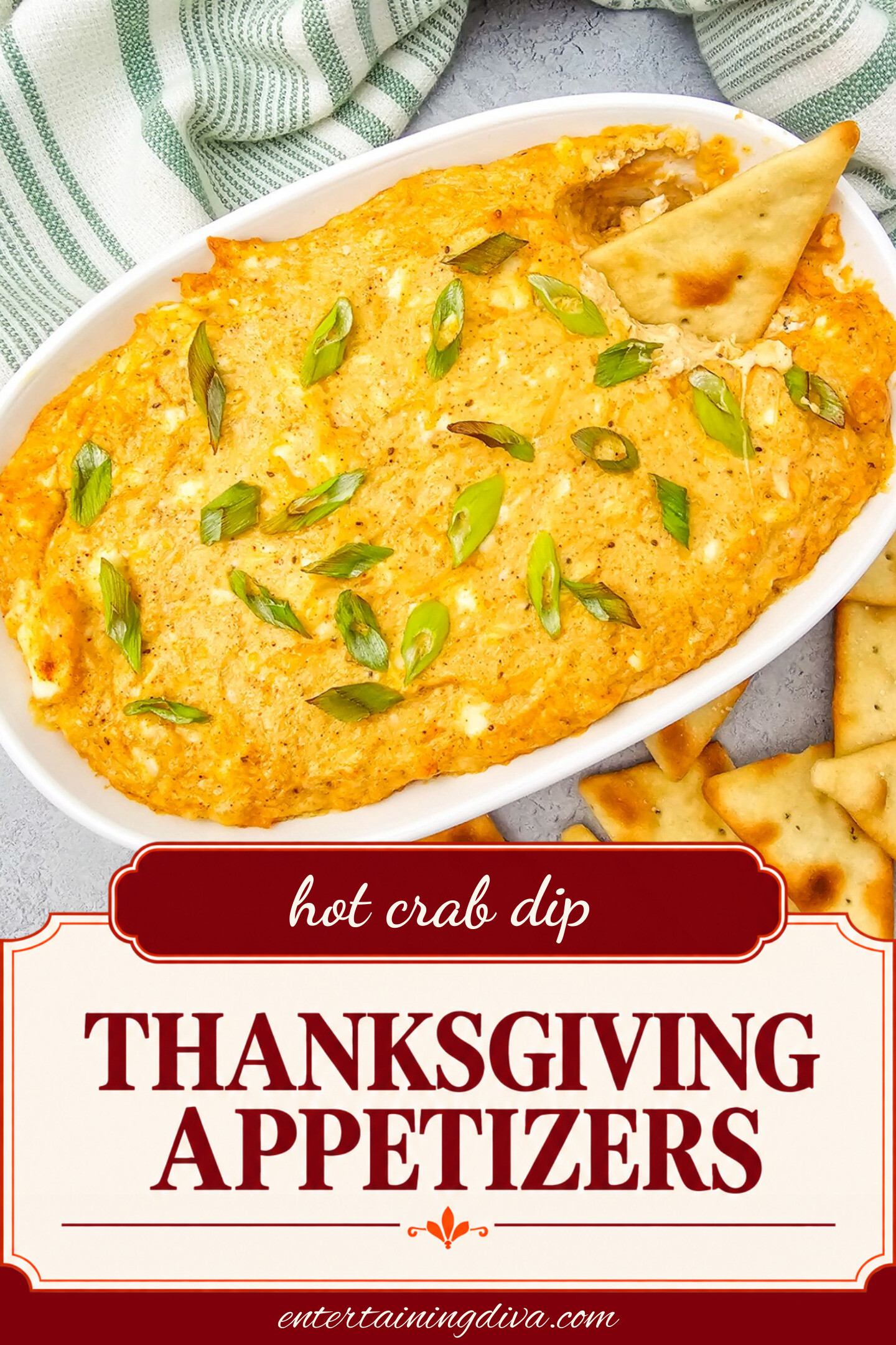Oval dish of creamy hot crab dip topped with sliced green onions, served with pita chips on the side and one chip dipped in the corner.