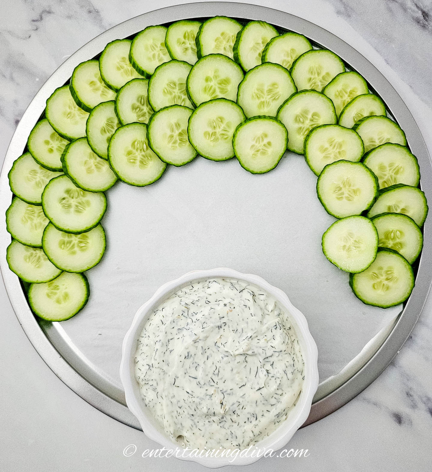 cucumbers around the edge of a plate with a bowl of dip
