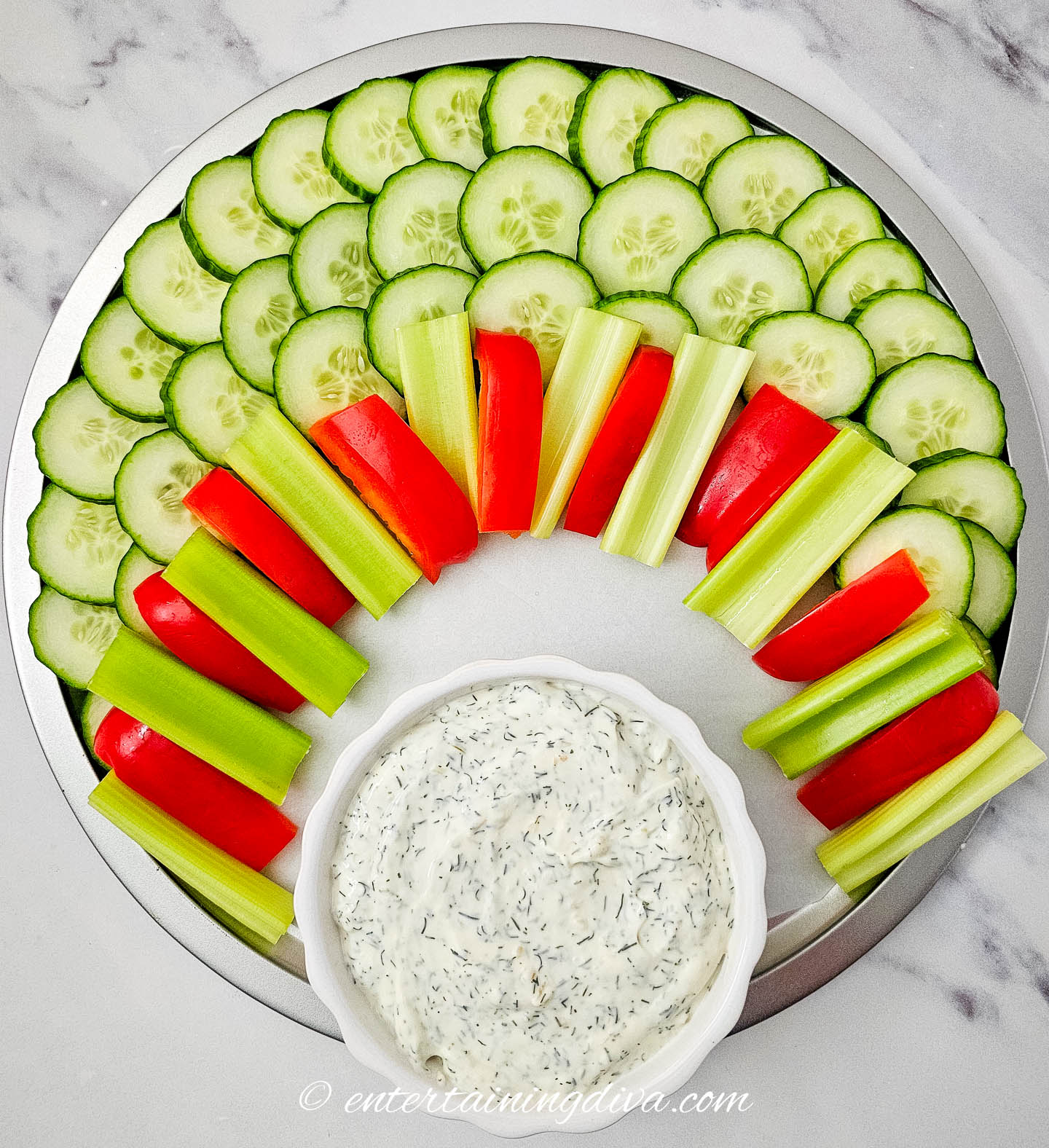 cucumbers, celery, and red peppers on a plate with a bowl of veggie dip